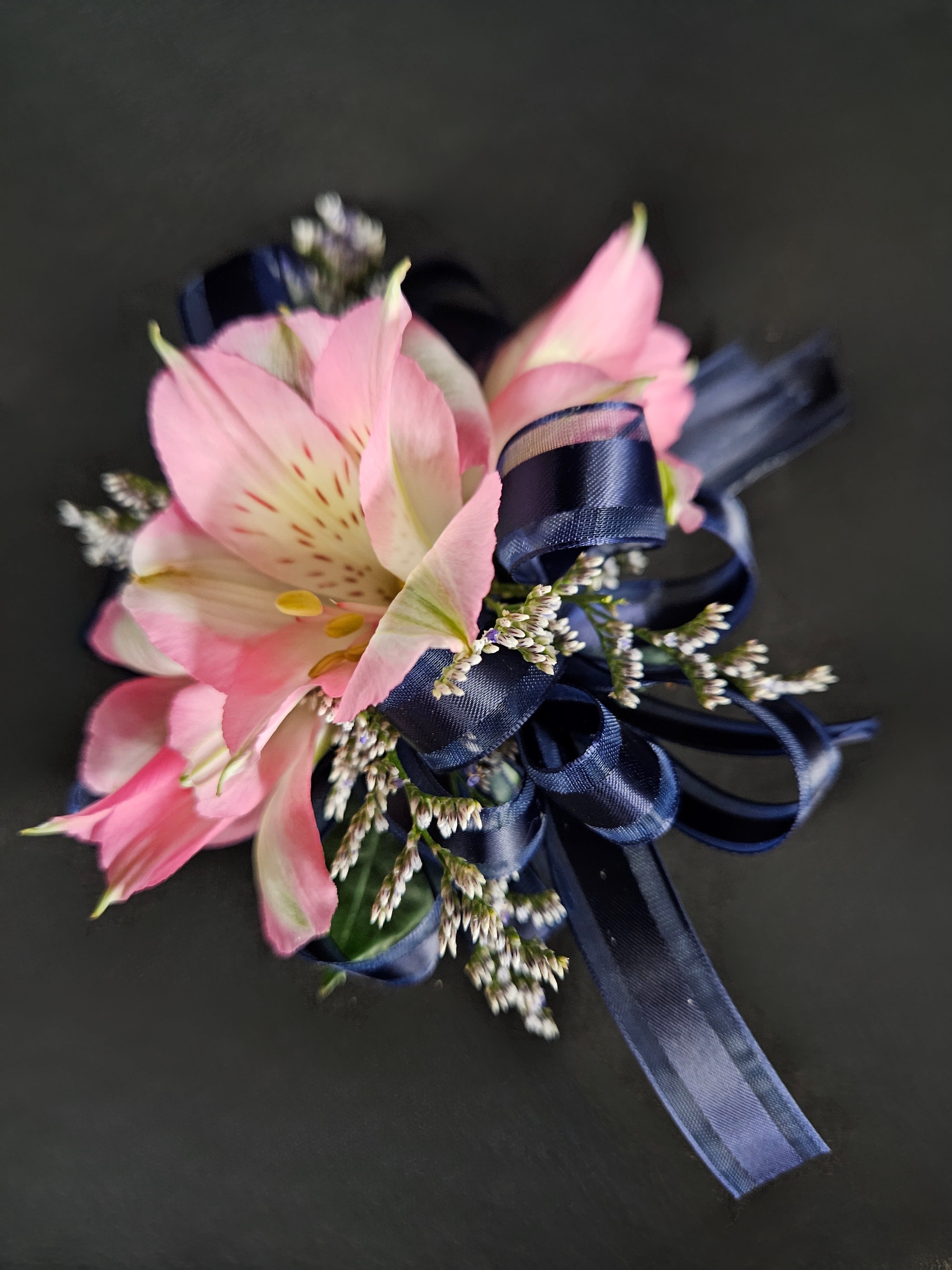 Pink alstroemeria corsage with navy ribbon on a dark background