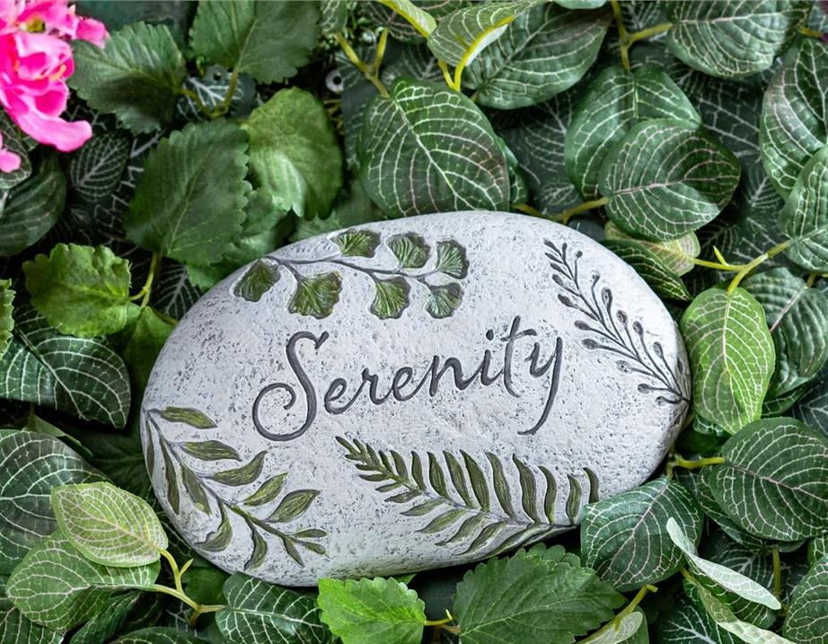 Decorative stone engraved with the word Serenity surrounded by green leaves