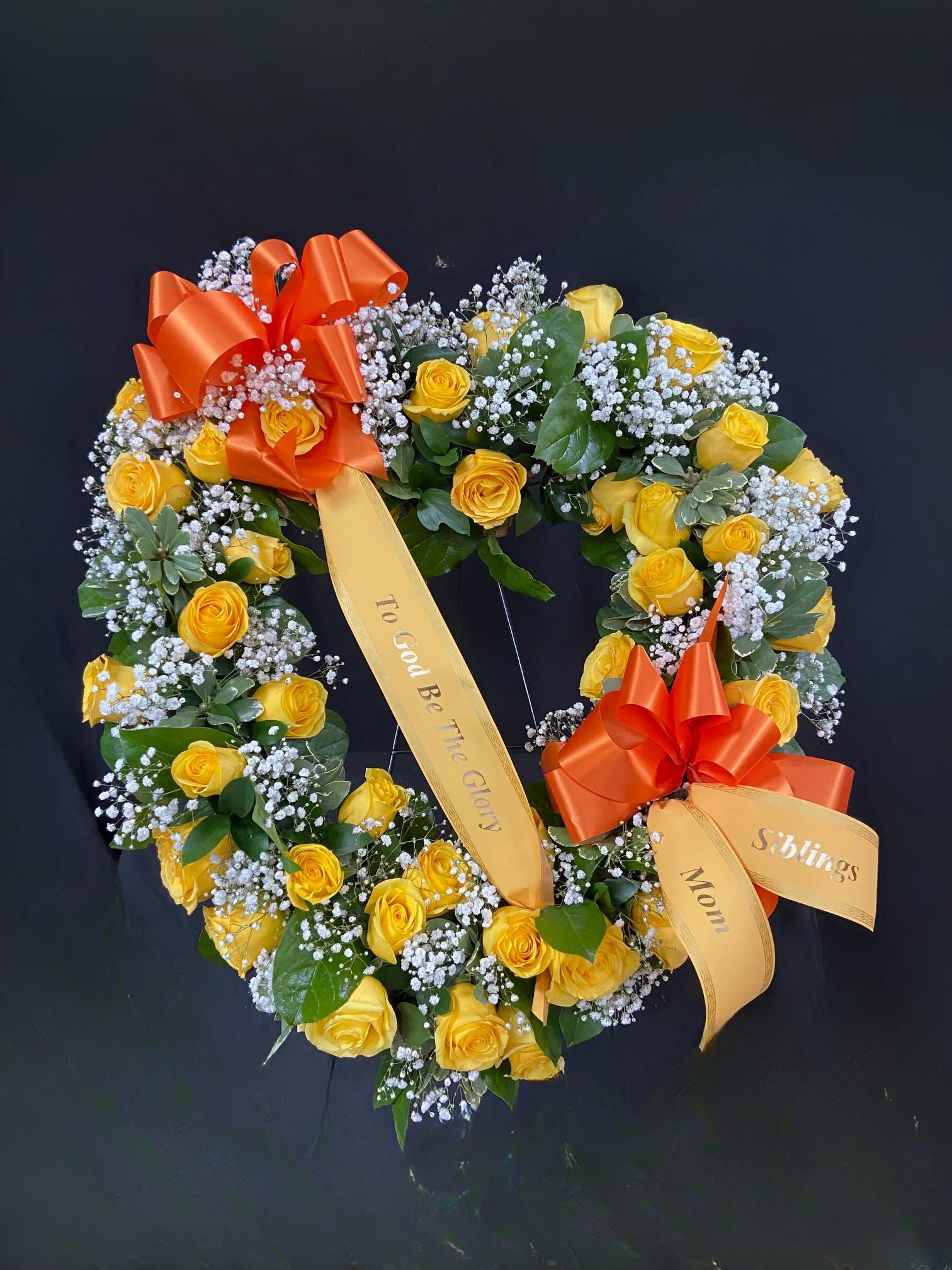 Heart-shaped wreath of yellow roses with orange ribbons on a dark background