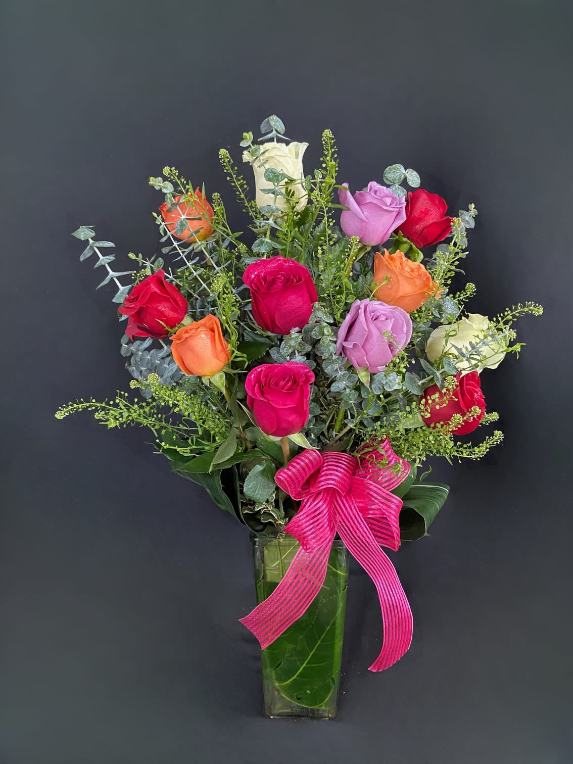 Mixed roses in a tall glass vase with a pink ribbon bow