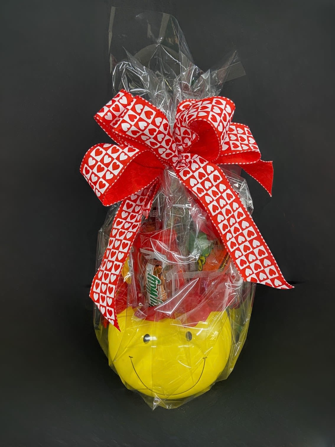 Gift basket wrapped in cellophane with a red heart ribbon and smiley-face container
