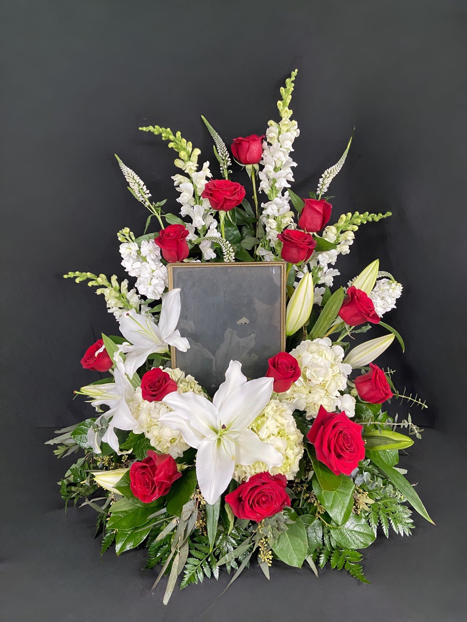 Missing You - Picture Frame Accent - Honor and celebrate the fruitful life of a lost loved one with an arrangement that truly encompasses their elegance. The Missing You memorial arrangement is a luxurious addition to any memorial service. Encompassing the picture of your choice, this arrangement features majestic white hydrangeas that will ease the minds and comfort the souls that are grieving with contrasting red roses to represent the vibrance of their life. Design is compatible with picture frames sizes approximating 12" H x 8" W. Picture Frame not included.