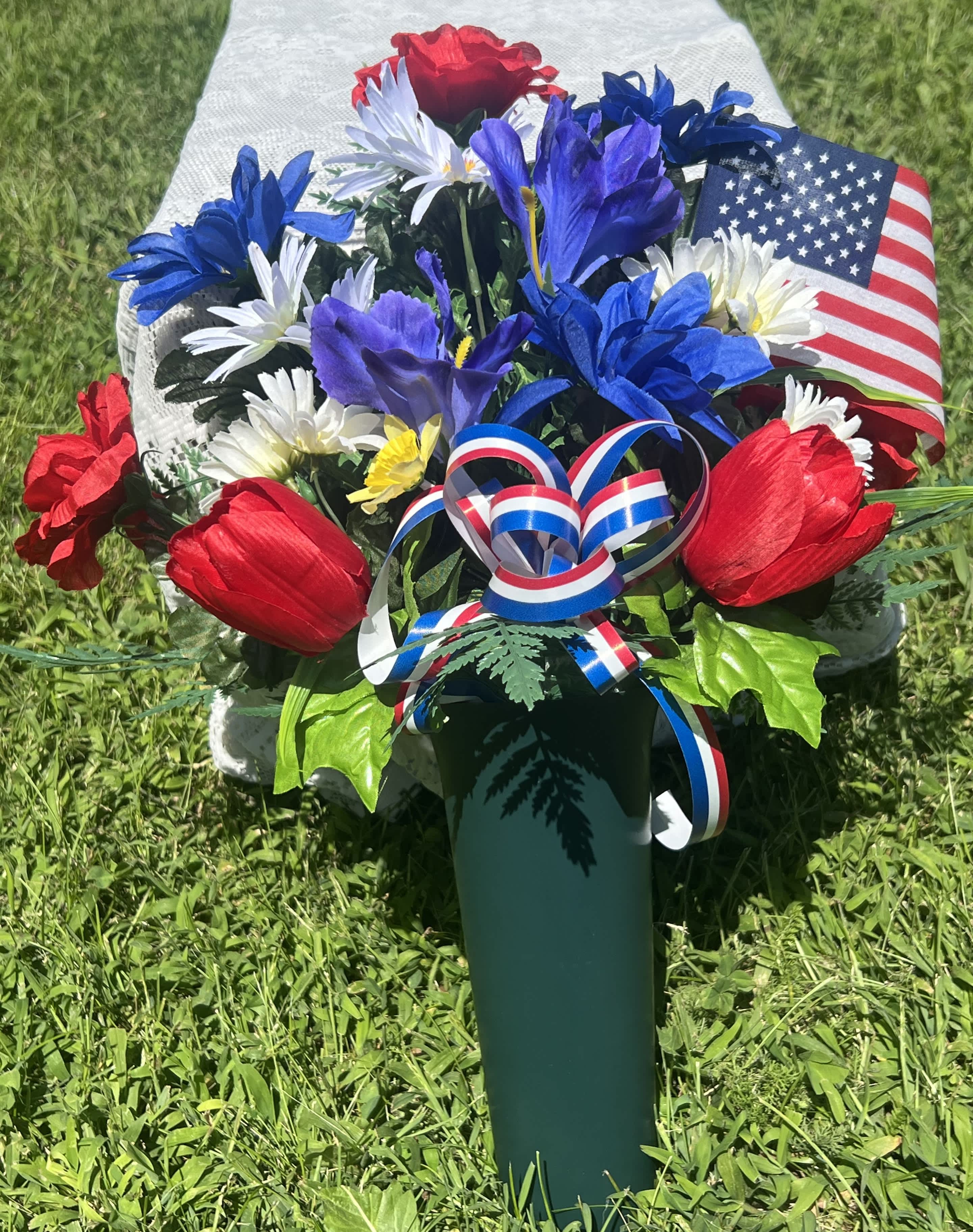 Red, white, and blue floral arrangement in a green vase with an American flag
