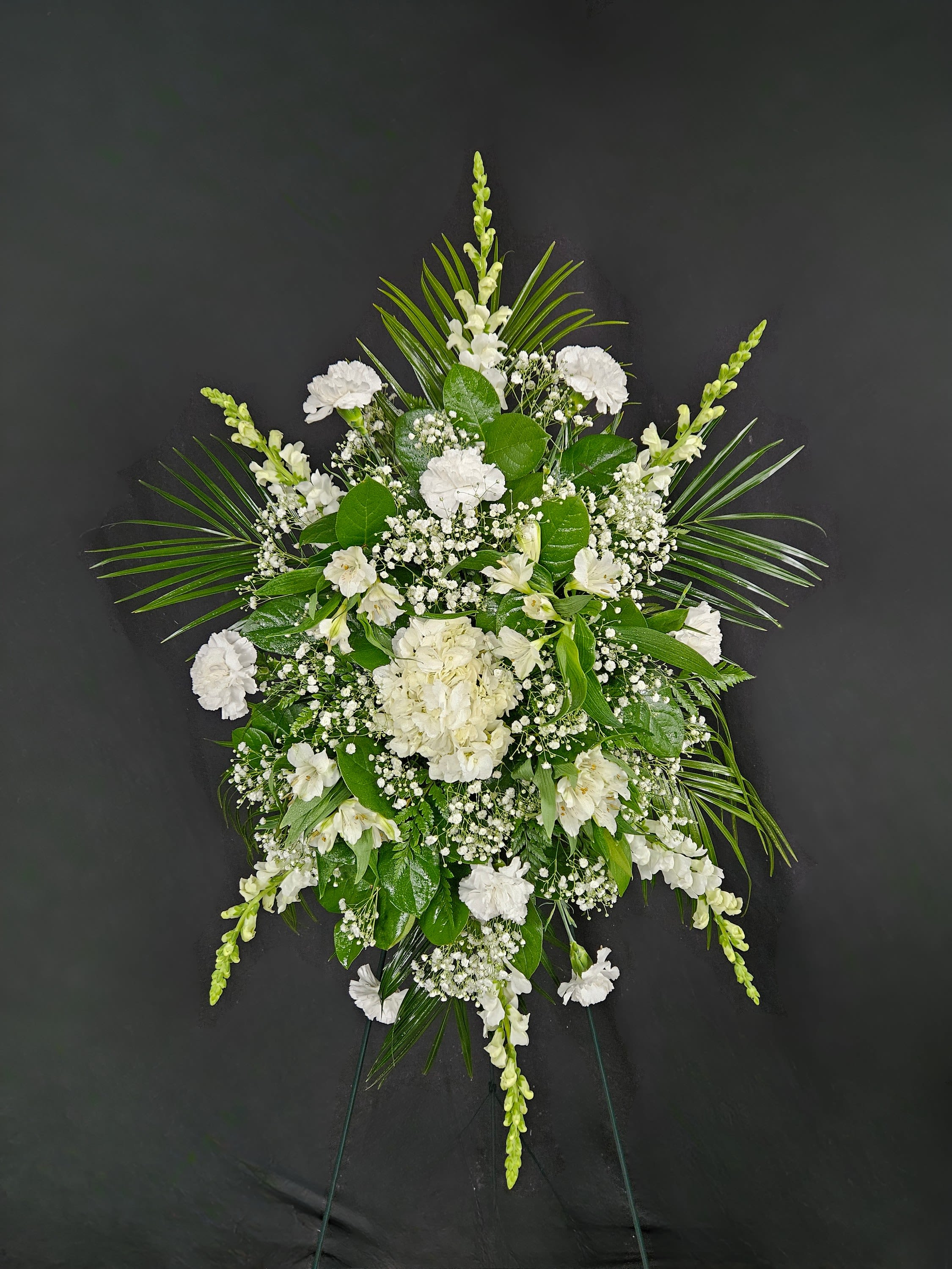 Mixed White Florals Standing Spray - A standing spray of assorted white flowers spread across a bed of greens. Arrangement is mounted on a 4.5ft standing easel for prominent display at funeral services.