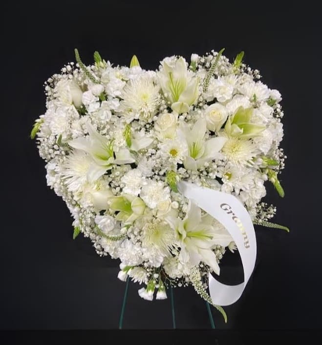 Heart-shaped standing arrangement of white flowers with a memorial ribbon on an easel.