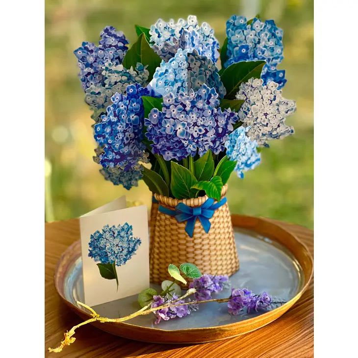 Blue and purple hydrangea-style silk flowers in a basket with matching card on a tray