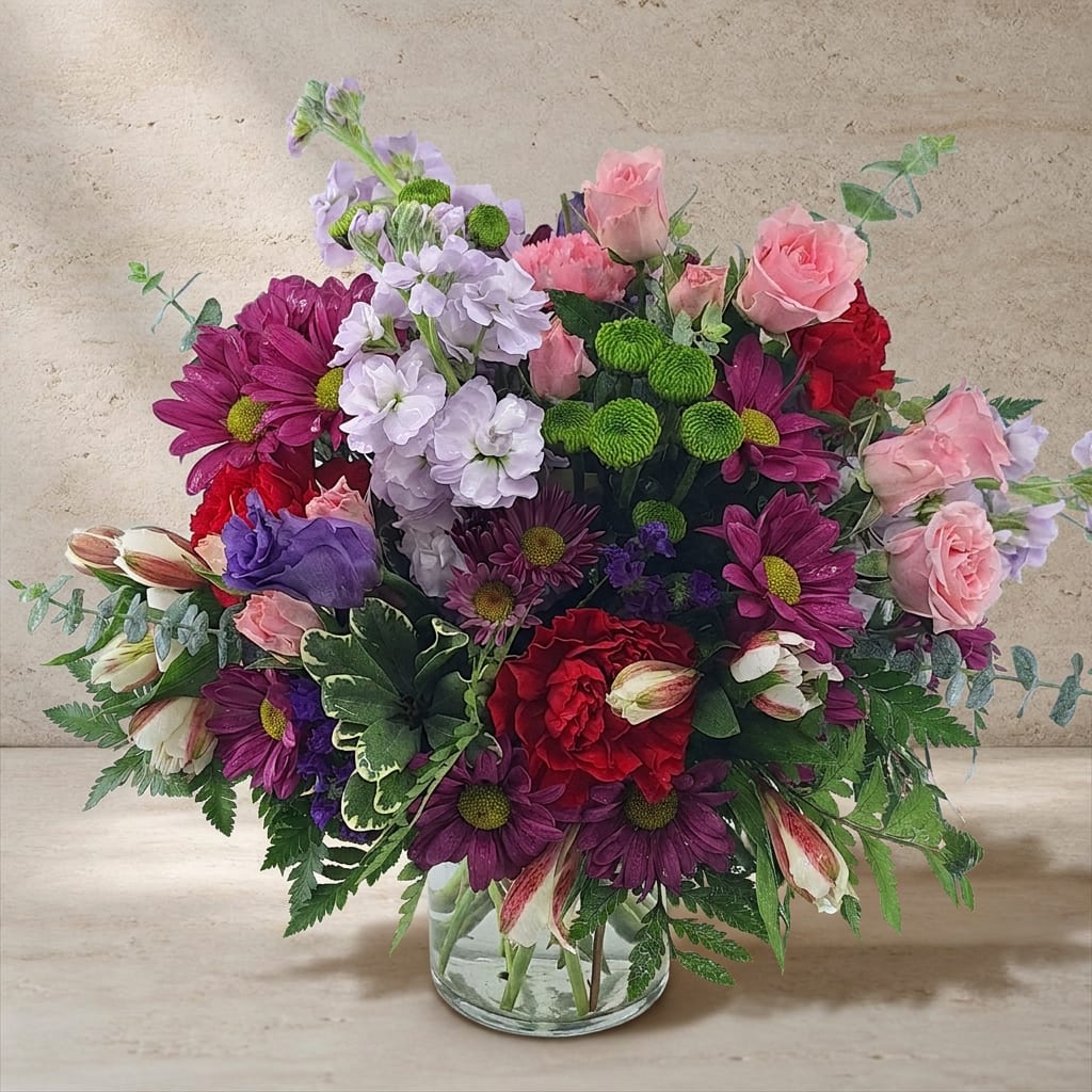 Mixed bouquet of pink, purple, red, and white flowers in a clear glass vase