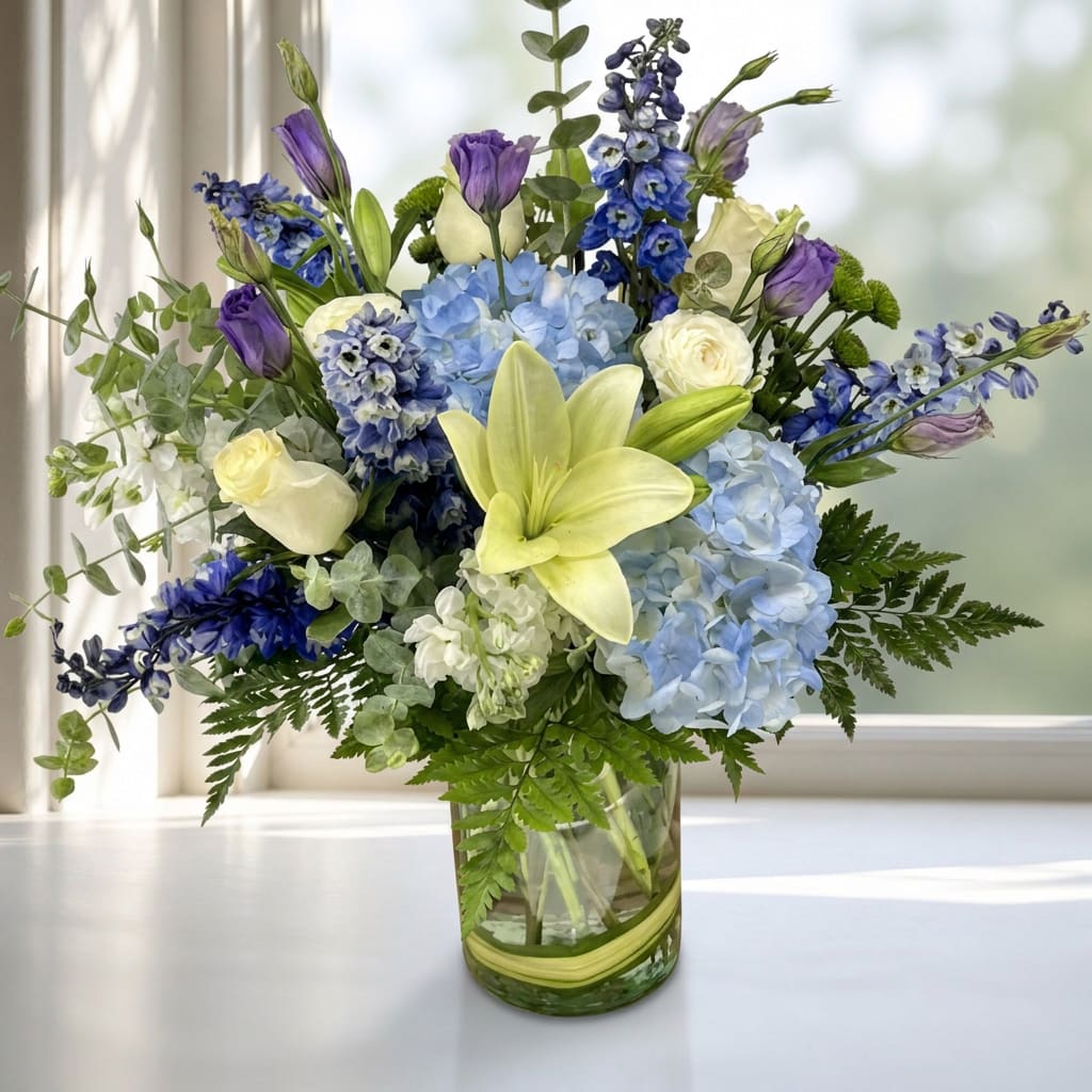 Blue and purple mixed bouquet with lilies and roses in a glass vase