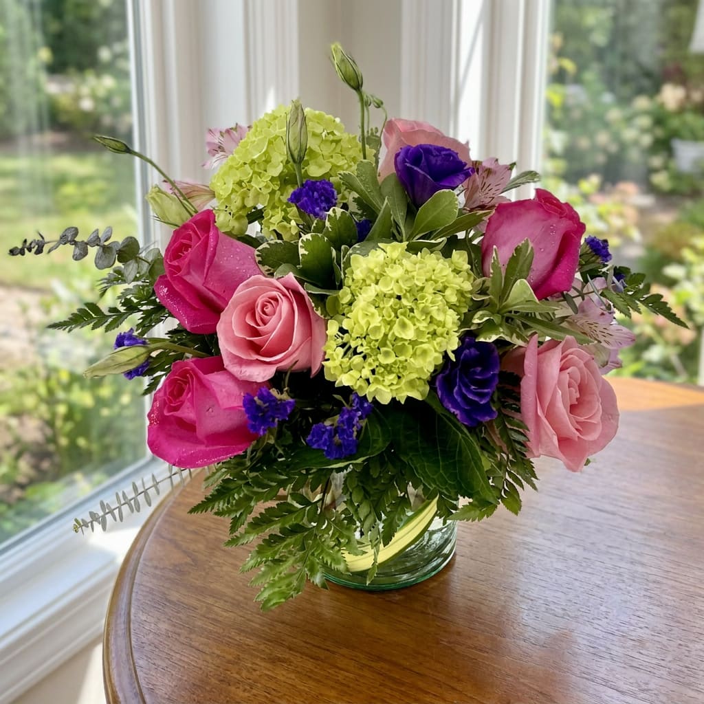 Bouquet of pink and purple roses with green hydrangeas in a glass vase