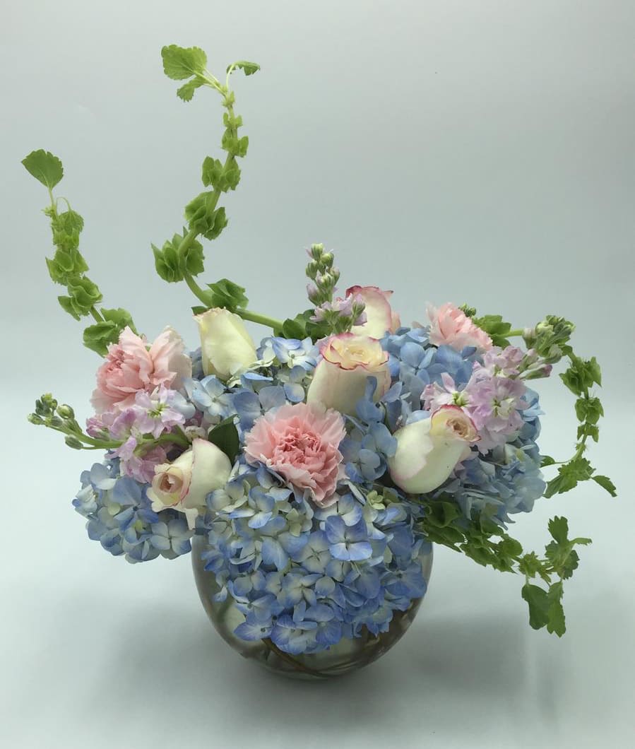 Blue hydrangea arrangement with pink carnations and white roses in a glass vase