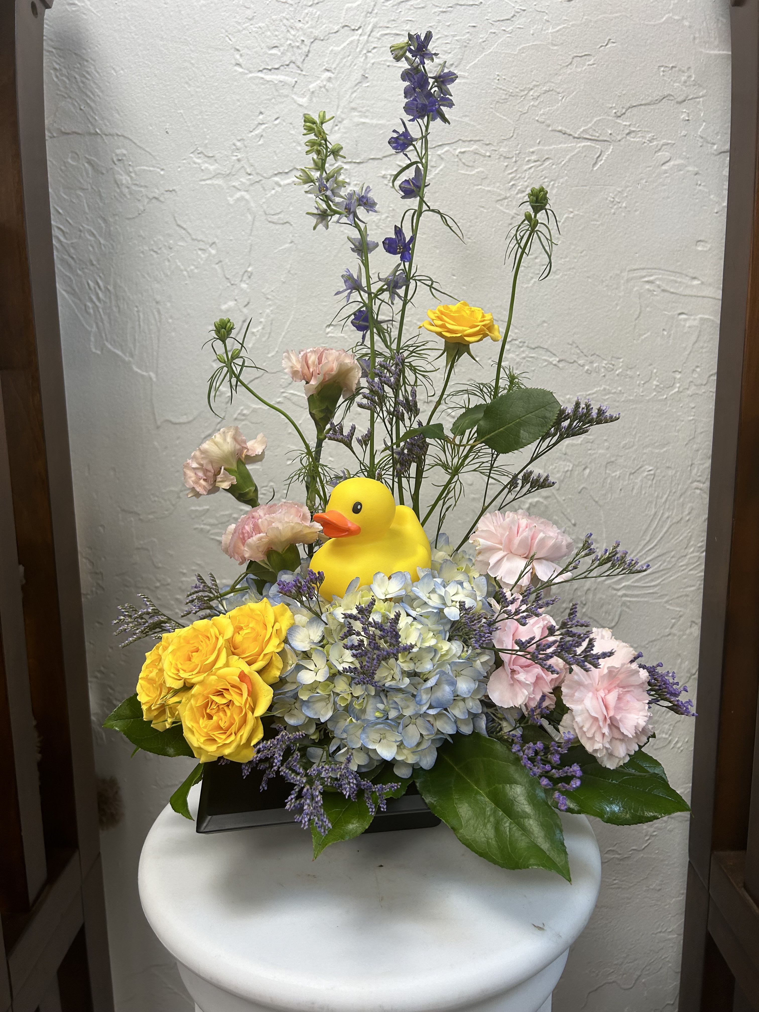 Floral arrangement with a yellow duck figurine in a black container