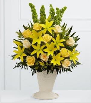 Yellow lilies and pale roses arranged in a cream pedestal vase