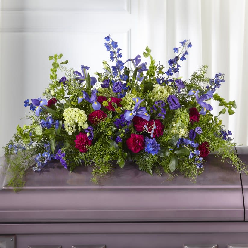 Large floral spray with blue, purple, pink, and white flowers on a casket