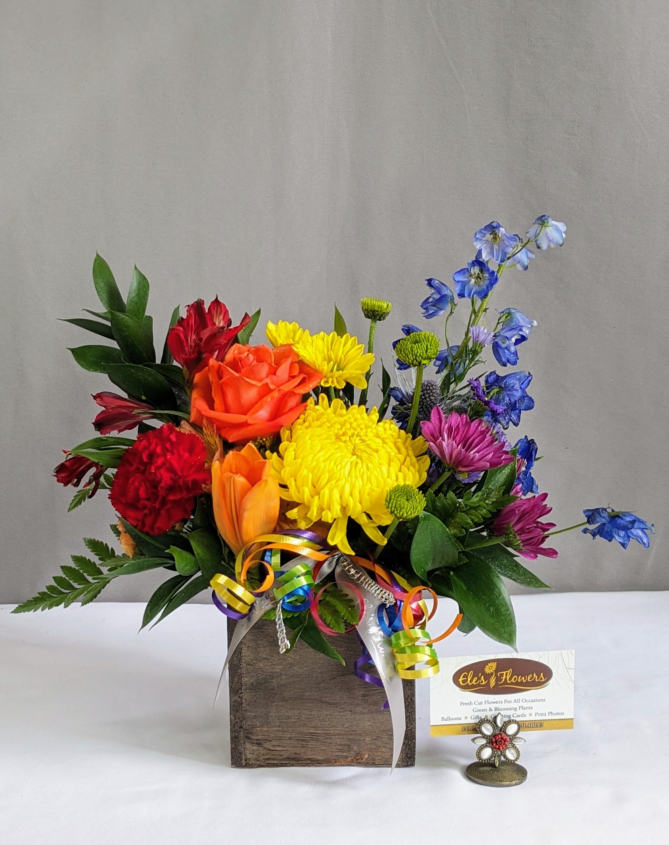 Over the Rainbow - Step into a world of vibrant beauty with our Over the Rainbow Arrangement. This stunning bouquet bursts with a kaleidoscope of colors, featuring a joyful mix of fresh blooms in every shade of the rainbow. From bright reds and oranges to vivid blues, purples, and sunny yellows, each flower is meticulously arranged to create a dazzling and uplifting display. Perfect for celebrating life's special moments or adding a burst of happiness to any space, it’s a radiant expression of joy and positivity. This design comes with a keepsake box or basket and is one sided.   The designs we create are custom and the blooms and containers will vary. We use the freshest product available to create the perfect floral combination for the recipient! If you have any special requests, please add those in the "special instructions" portion of your order to help us dial in your vision. Otherwise, our skilled designers, Sara, Brett &amp; Betty will take it from here! Please note that the photos are examples of our creations only – floral selection will vary based on what is available.  Approximate Dimensions:  Standard Size: 14"H x 10"W