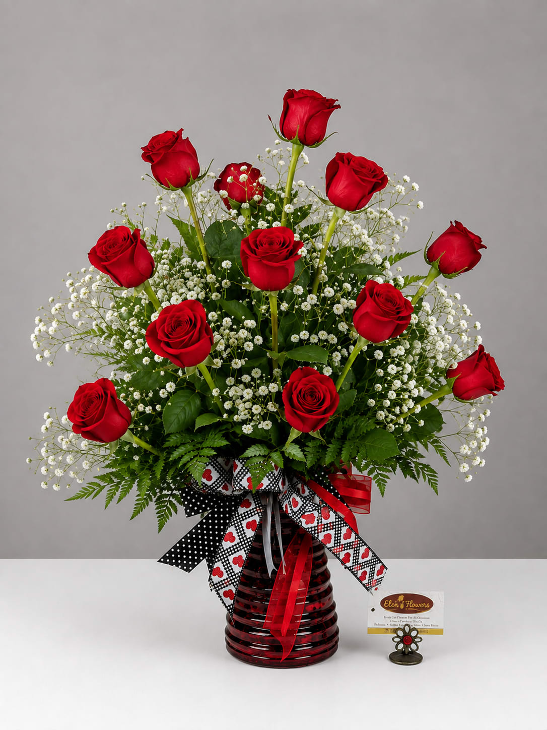 Red roses arranged in a red glass vase with white filler flowers