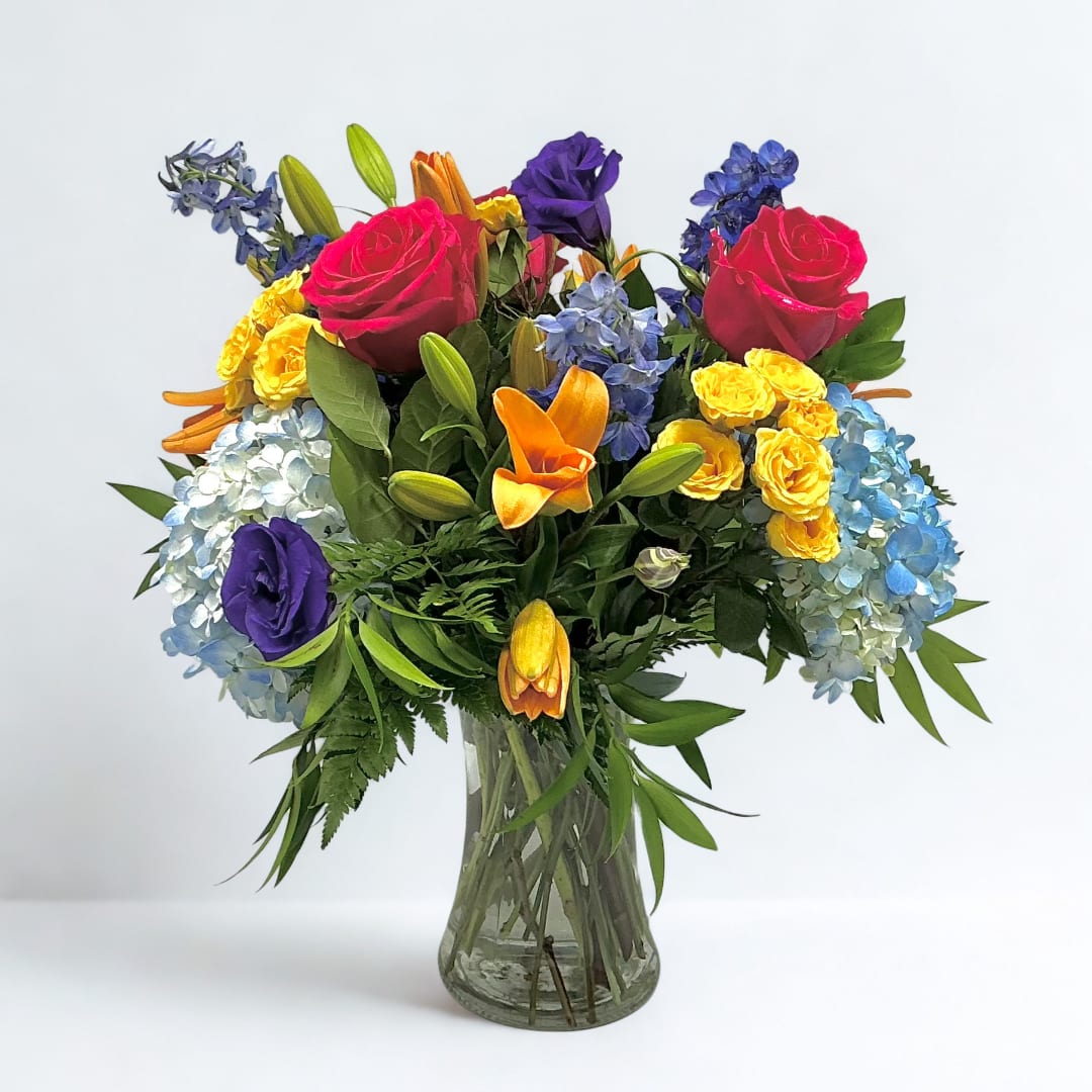 Colorful bouquet of roses, lilies, and hydrangeas in a clear glass vase