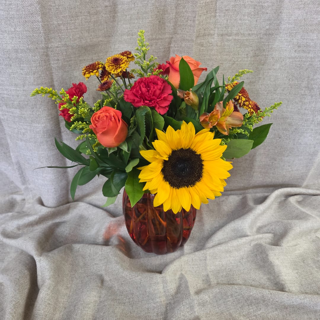 Mixed bouquet with a sunflower, roses, carnations, and alstroemeria in a red glass vase