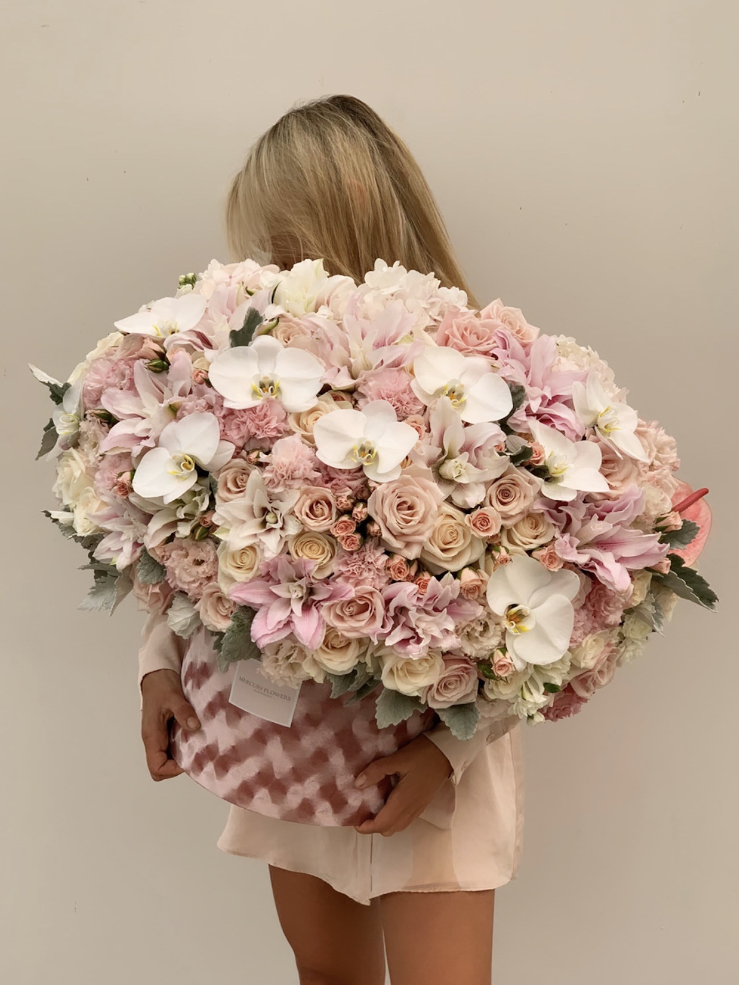 Large pastel bouquet of roses, orchids, and white blooms in a pink patterned box