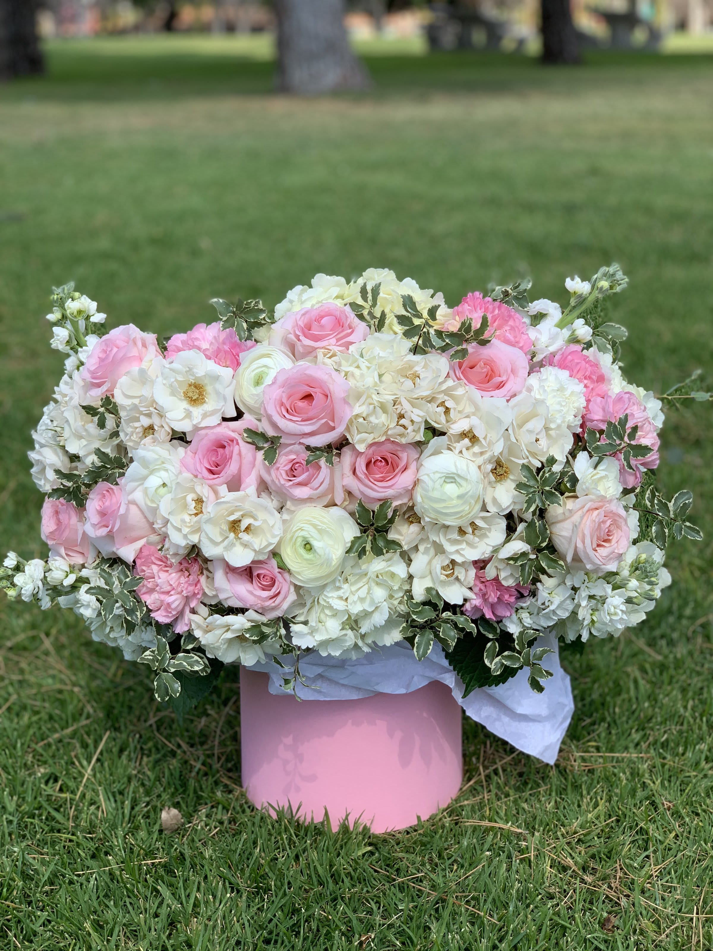 Pink and white floral arrangement in a pink box on grass