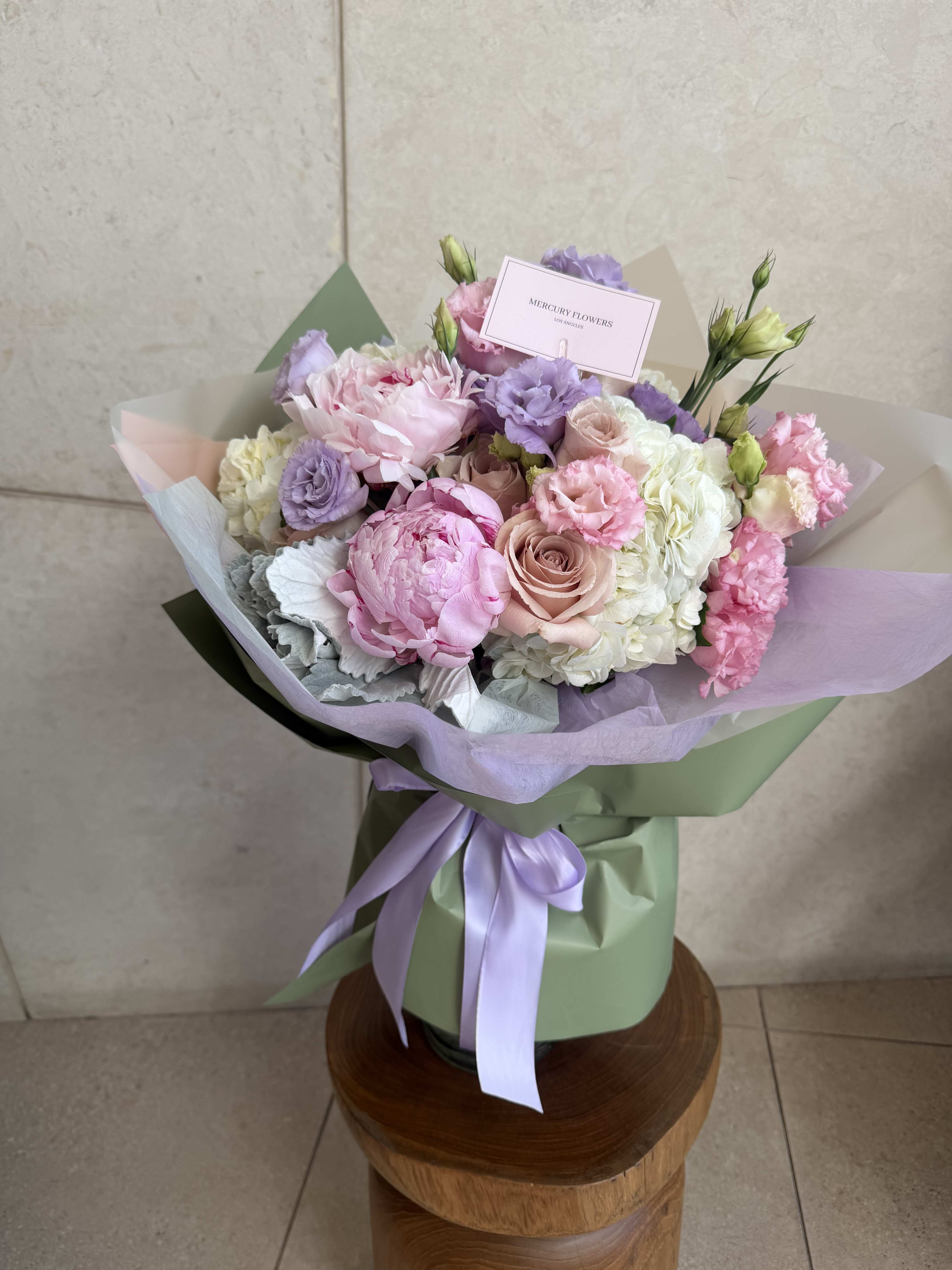 Pastel bouquet of pink, lavender, and white flowers wrapped in green paper