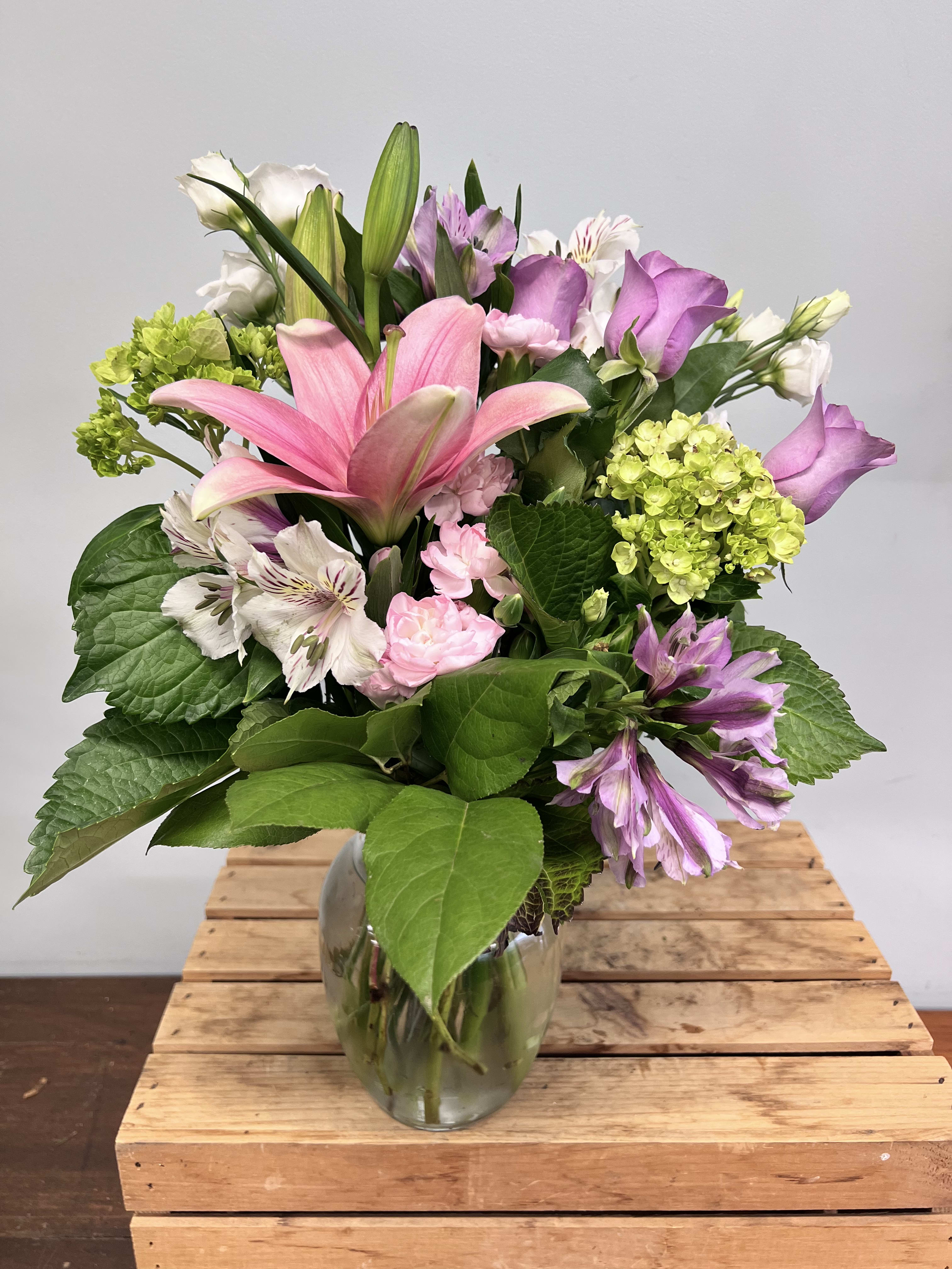 Pink lilies and purple flowers in a glass vase
