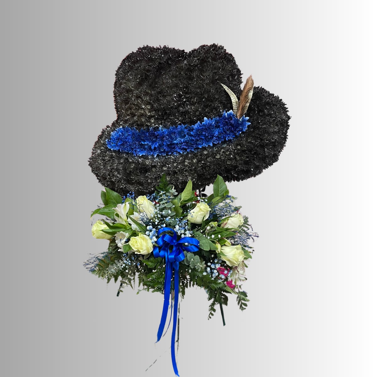 Black floral hat-shaped arrangement with blue ribbon and pale roses