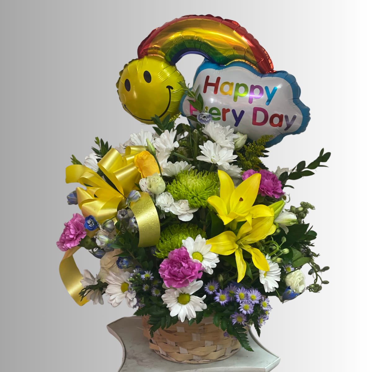 Basket arrangement of mixed flowers with rainbow and smiley balloons