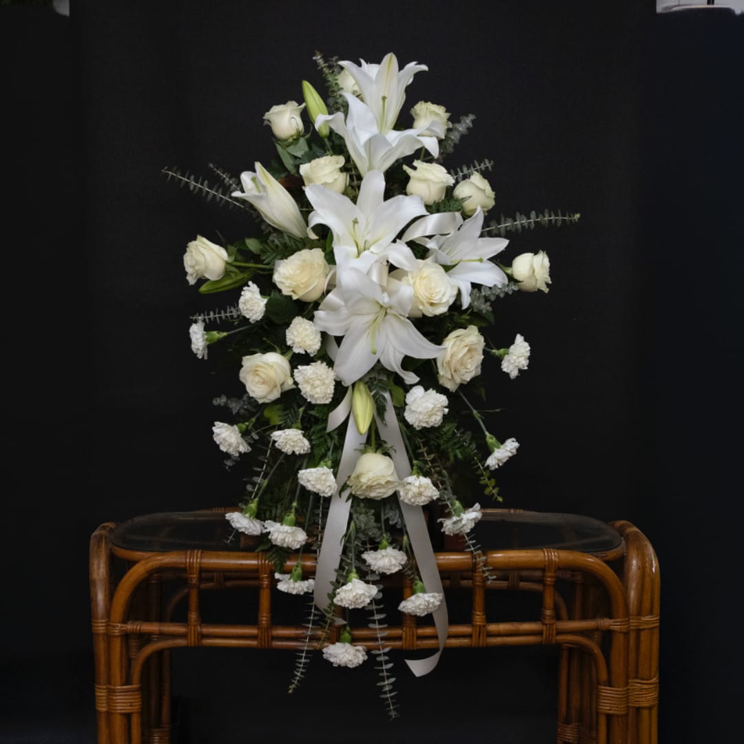 White lilies and roses arranged in a tall standing spray with ribbon