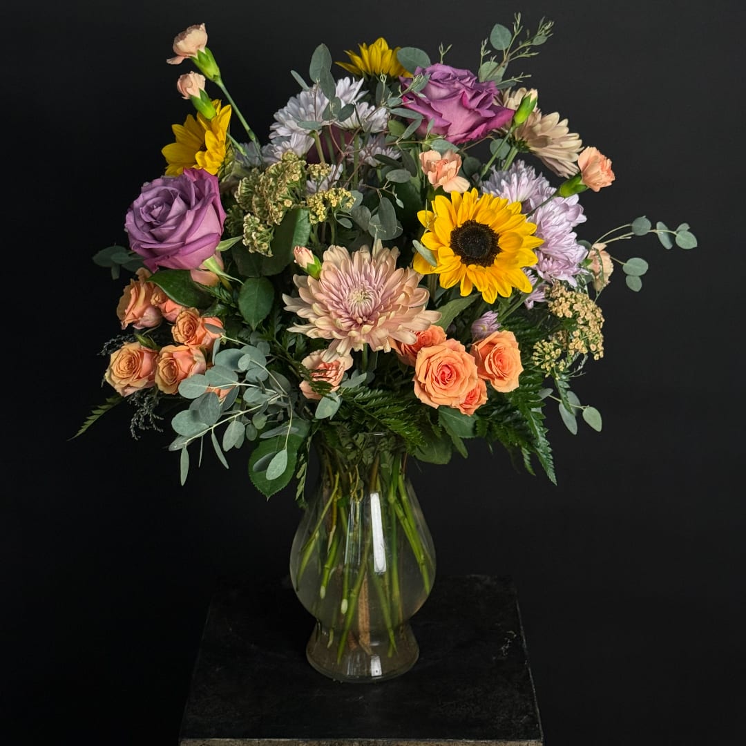 Mixed bouquet of roses, sunflowers, and chrysanthemums in a glass vase