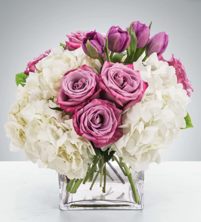 Pink roses and purple tulips arranged with white hydrangeas in a clear glass vase