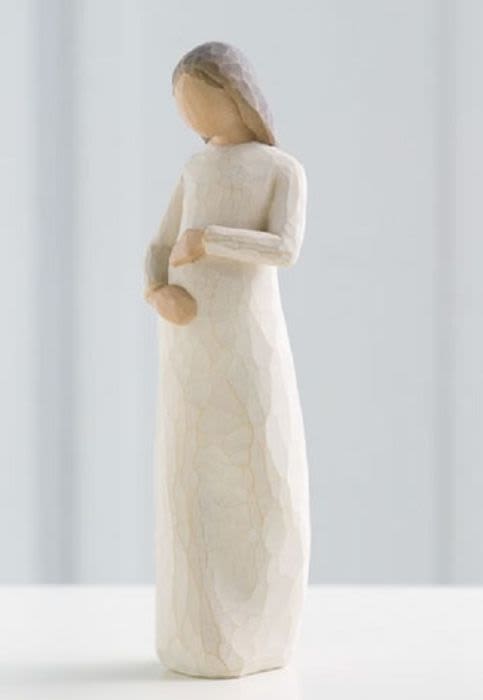 Carved wooden figurine of a woman in a long cream dress holding her belly