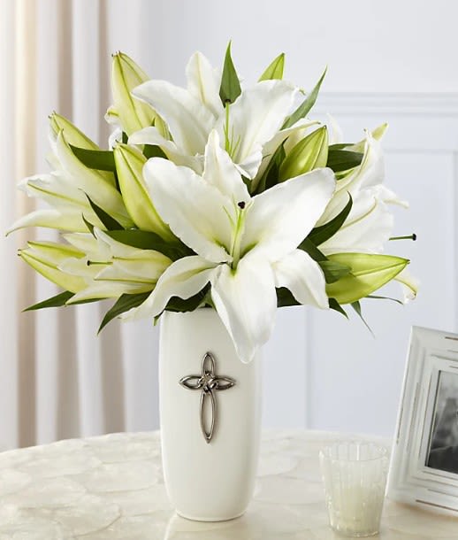 White lilies arranged in a tall white vase with a cross emblem