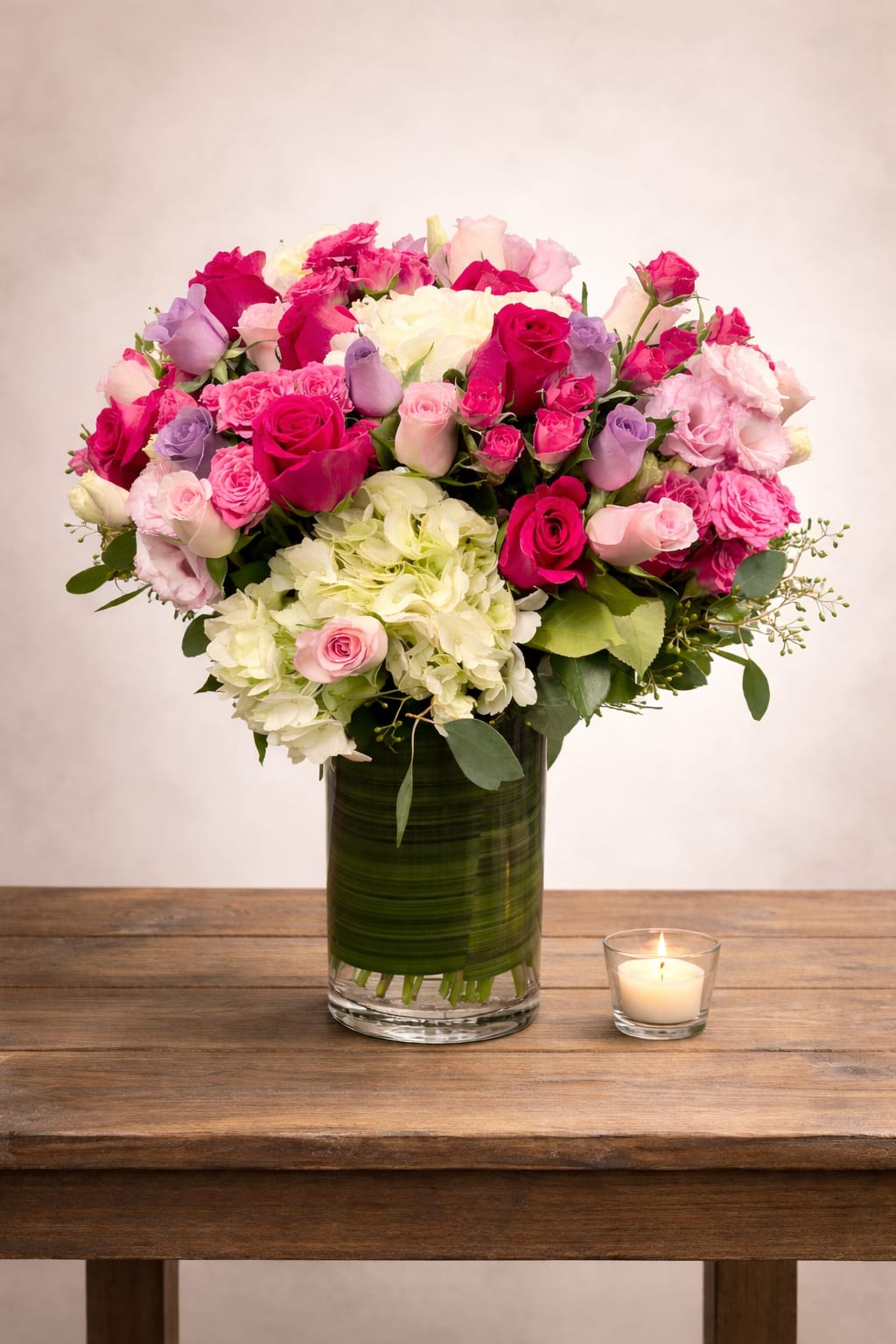 Pink and white rose bouquet in a glass vase beside a lit candle