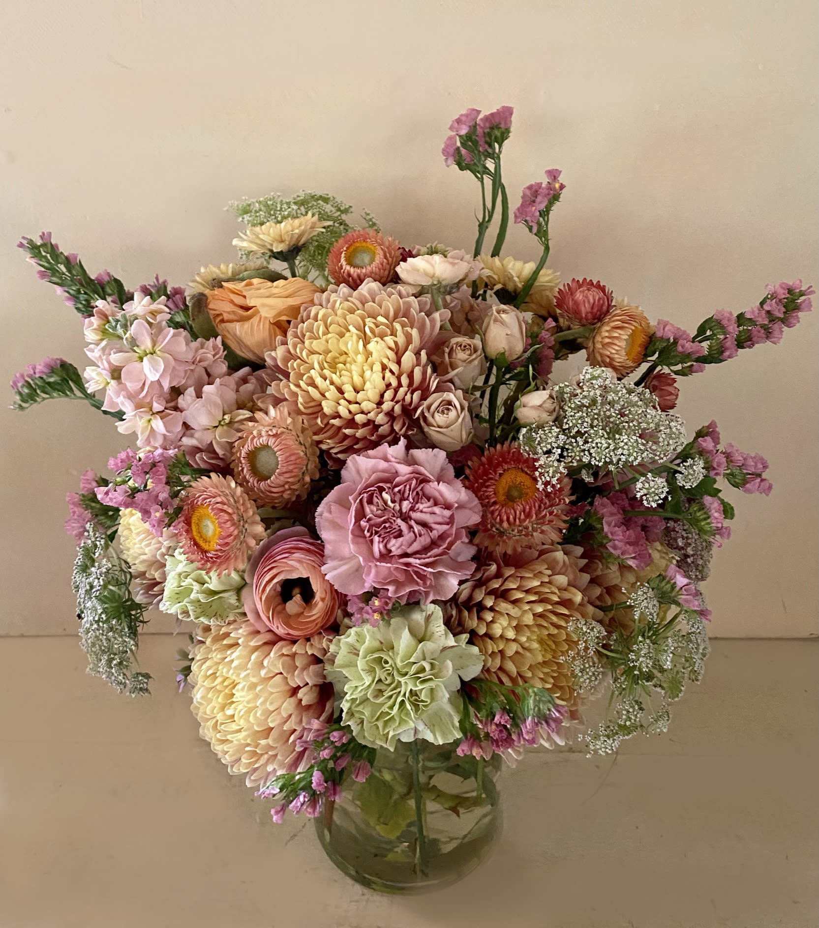 The Golden Lady - Send some Holiday cheer in a very pretty slighty tall arrangement of Golden brown, orange and coral colors arranged with stems like crysantemums, ranuculus, carnations and other sesonal flowers in golden colors. Fitted for the Family gathering this Holiday season. Placed in a 5" by 7" clear vase.Choose Deluxe for more stems.