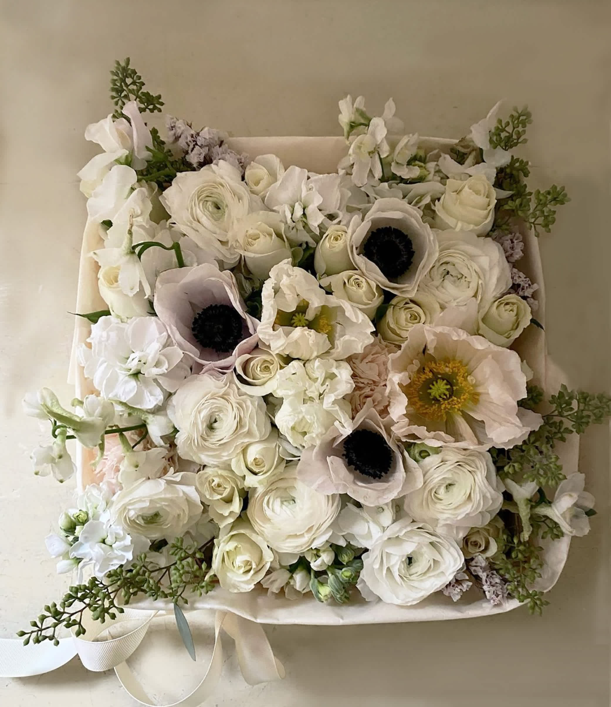 White floral bouquet with pale pink anemones and roses in a square wrap