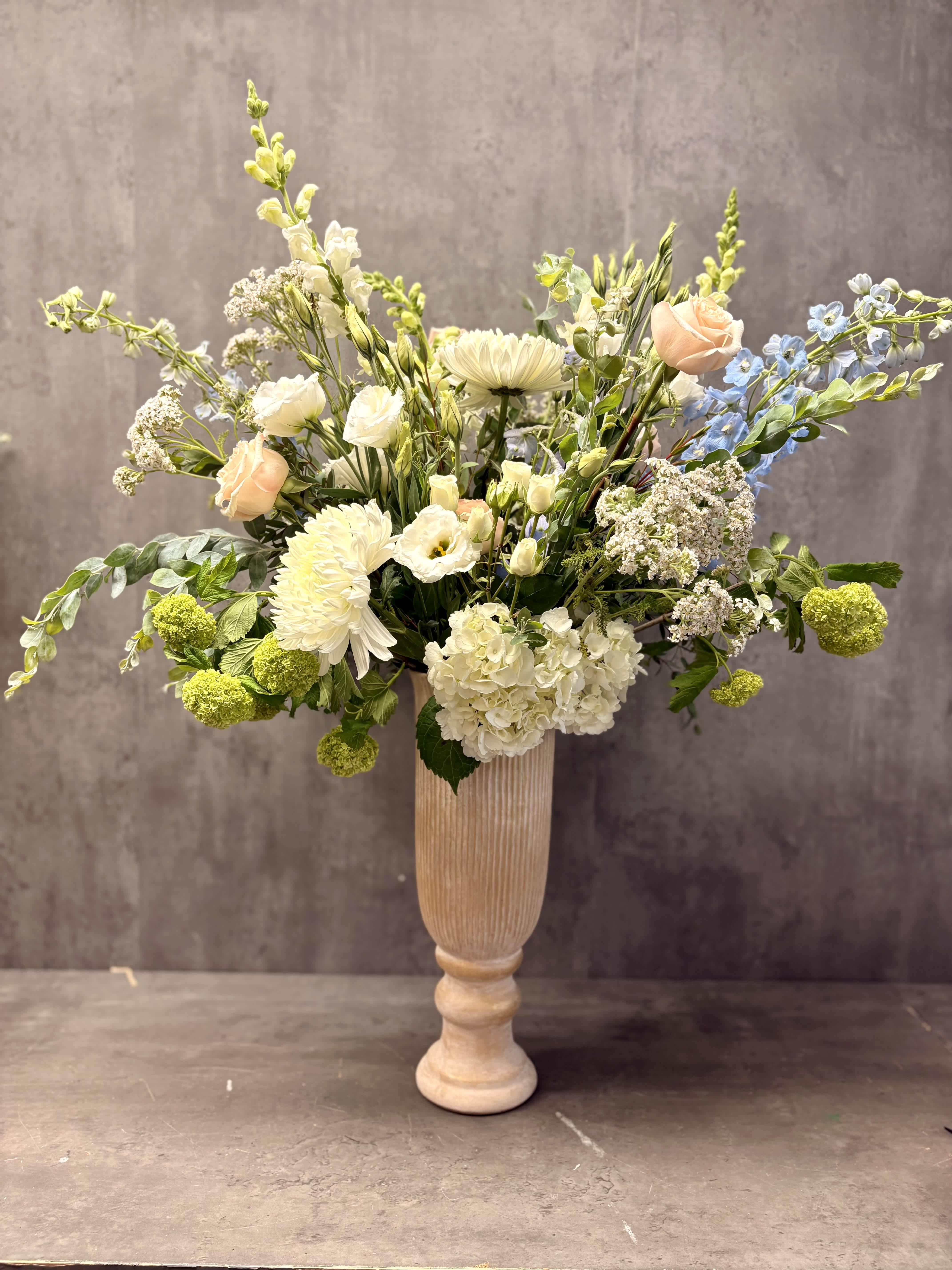 Tall floral arrangement in a pedestal vase with white, peach, and blue blooms