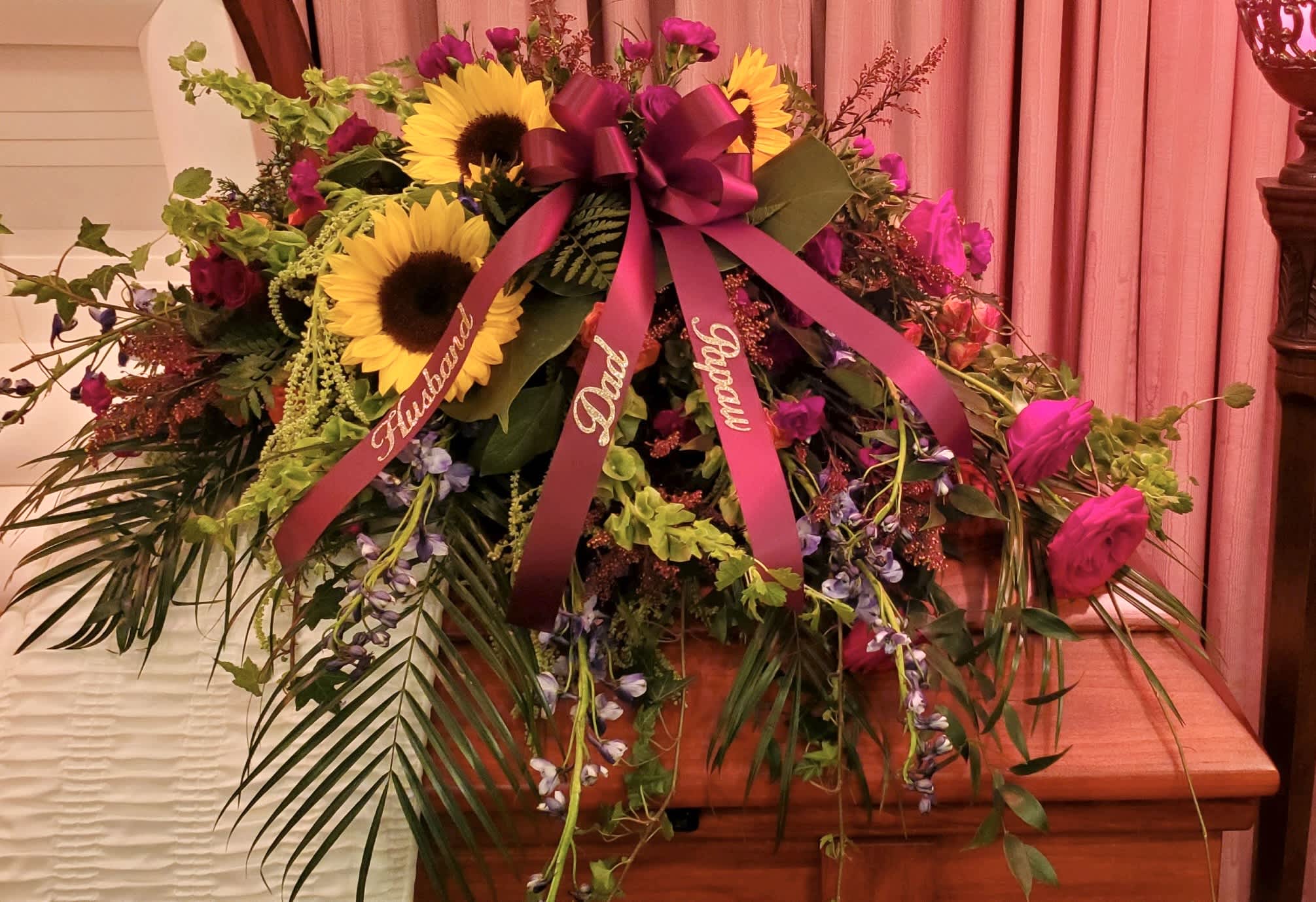 Large floral spray with sunflowers, pink roses, and ribbons