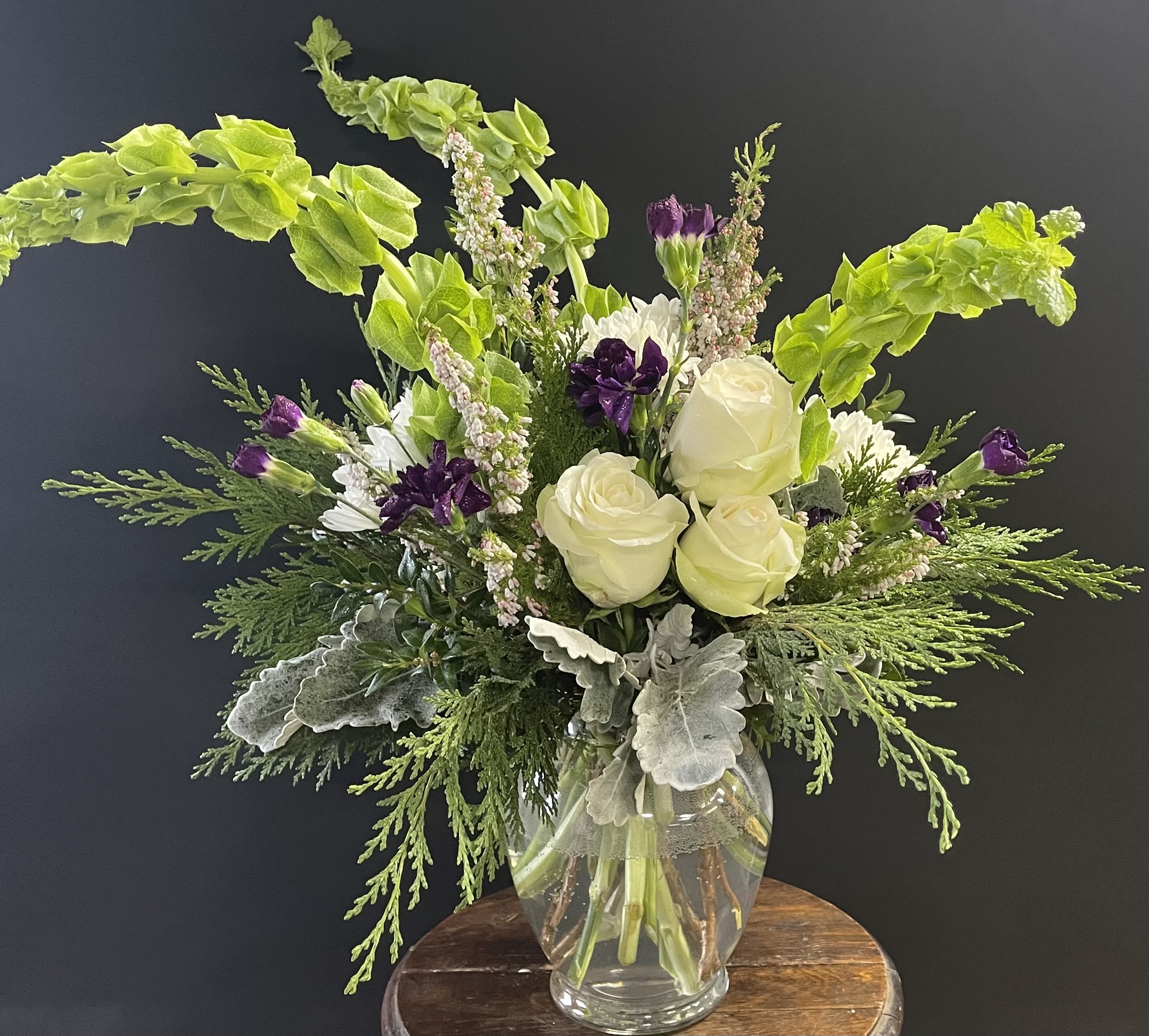 White roses and purple flowers in a clear glass vase with bright green foliage