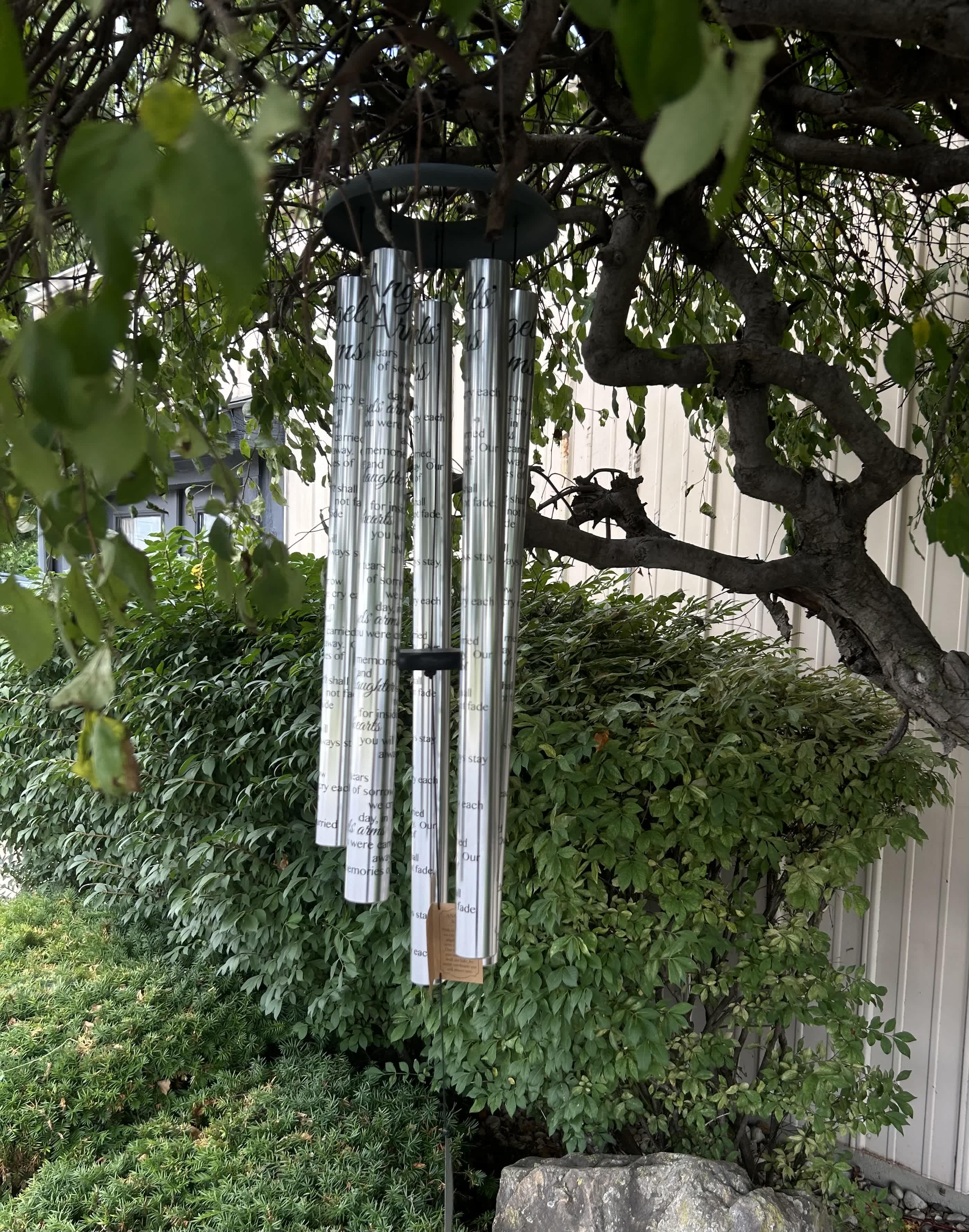 Silver memorial wind chimes hanging from a tree in a garden
