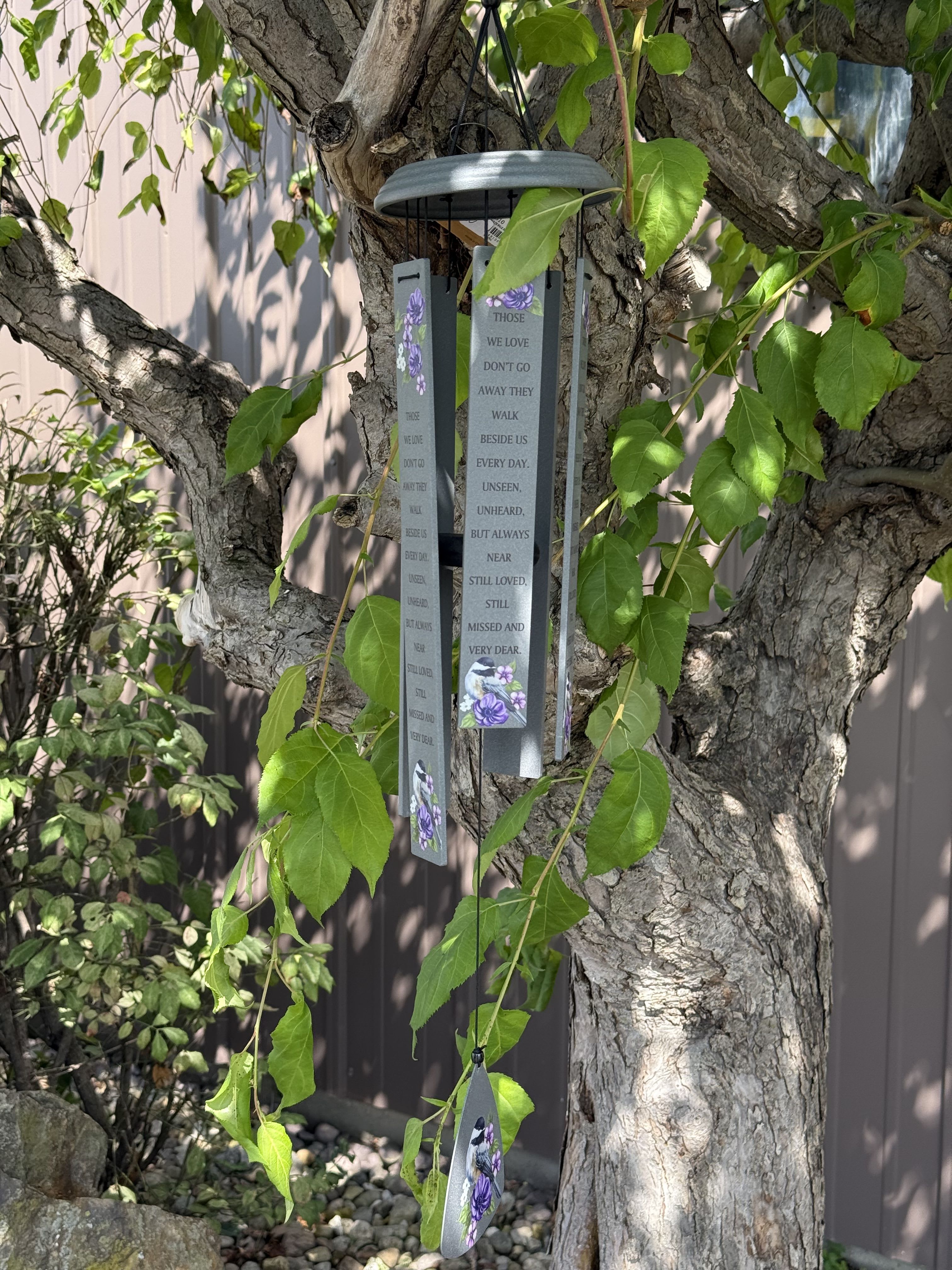 Hanging memorial wind chime with purple floral accents on a tree