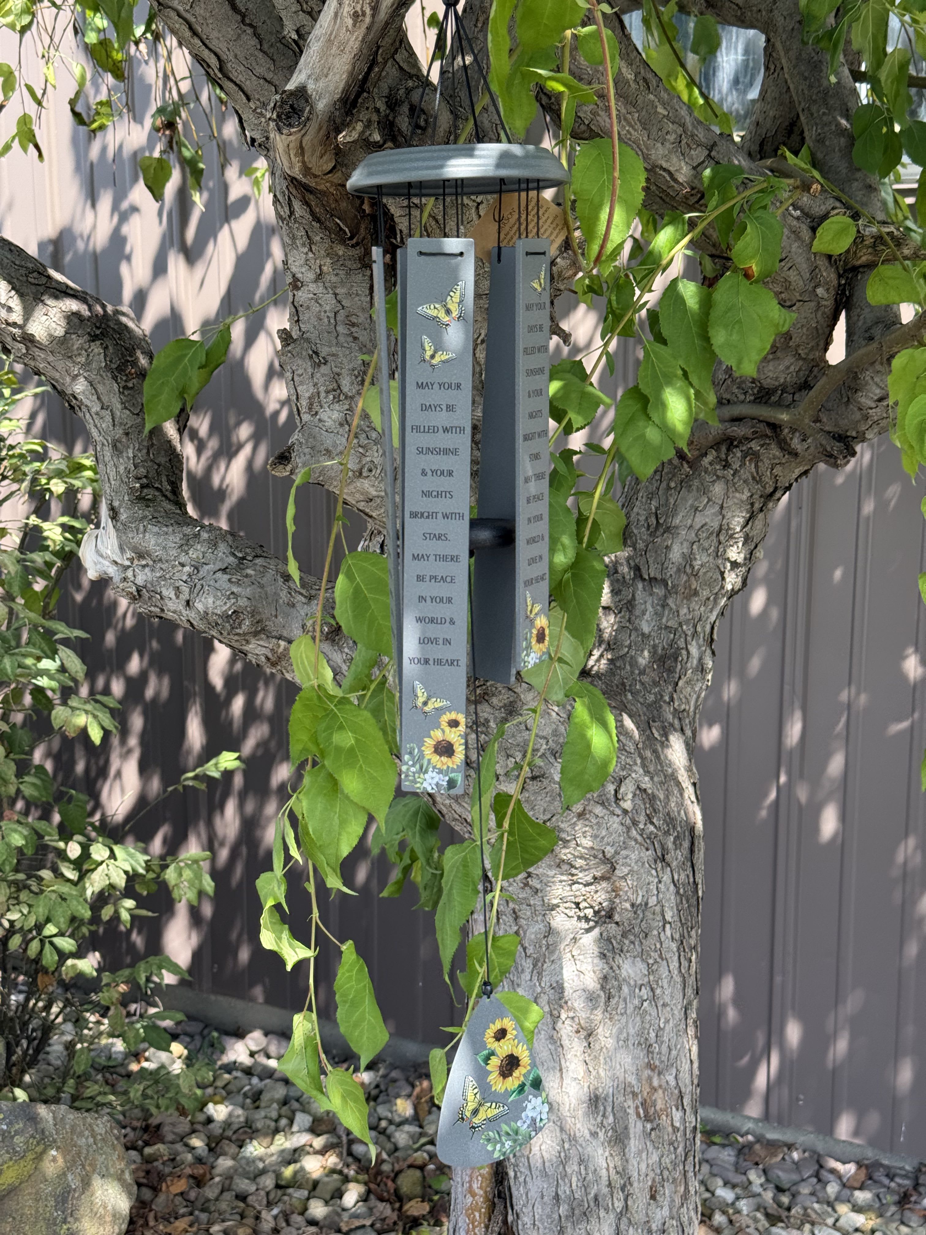 Hanging metal wind chime with butterfly and sunflower designs on a tree
