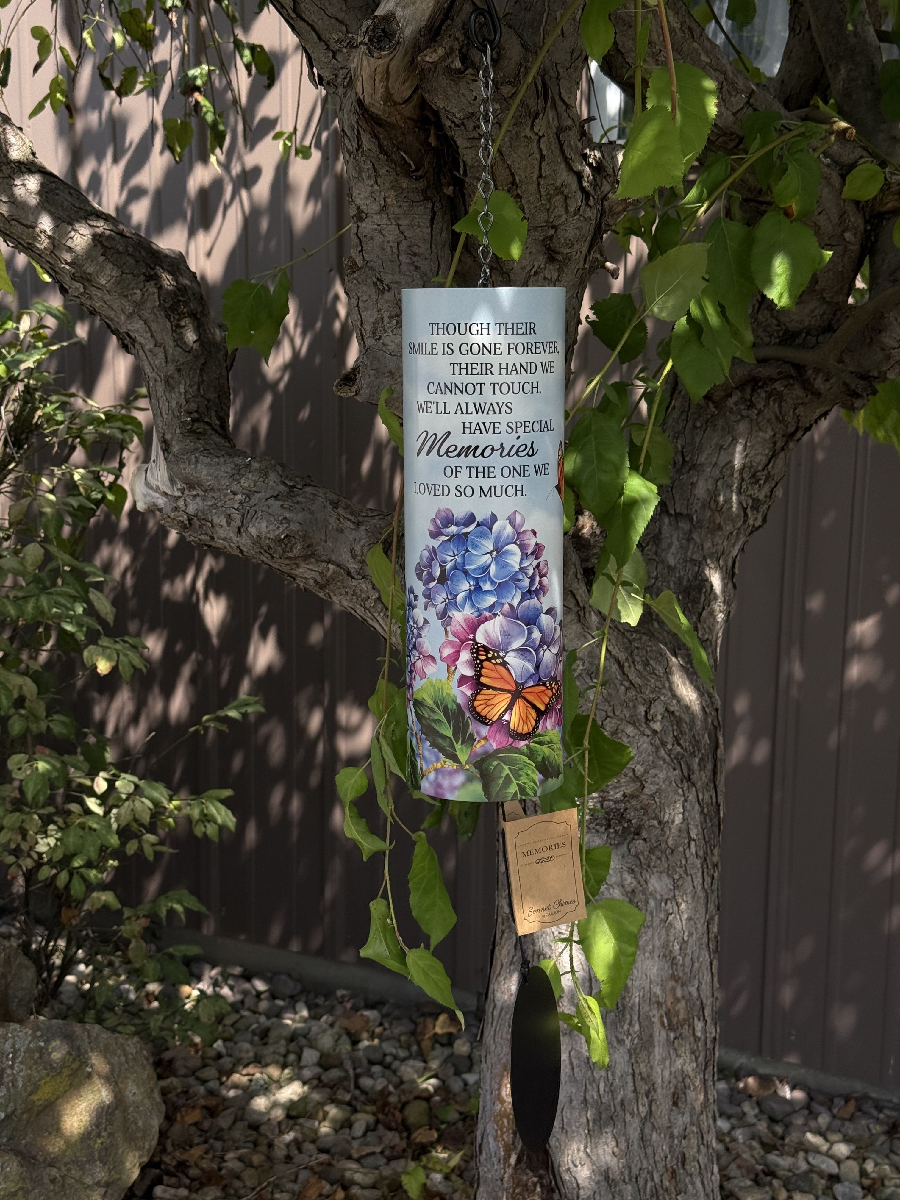 Memorial wind chime hanging from a tree with floral and butterfly artwork