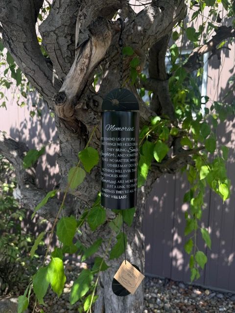 Black memorial wind chime hanging from a tree branch