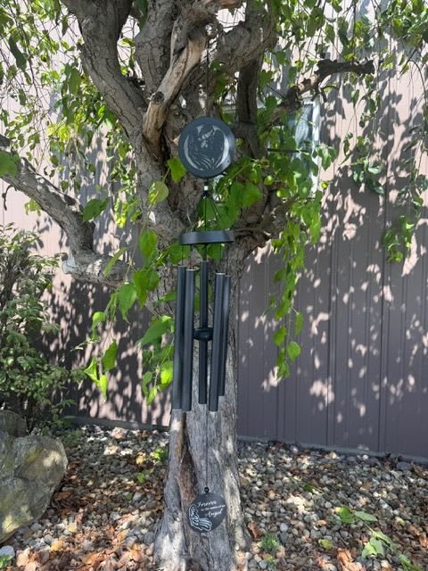 Black wind chime hanging from a tree trunk in a yard