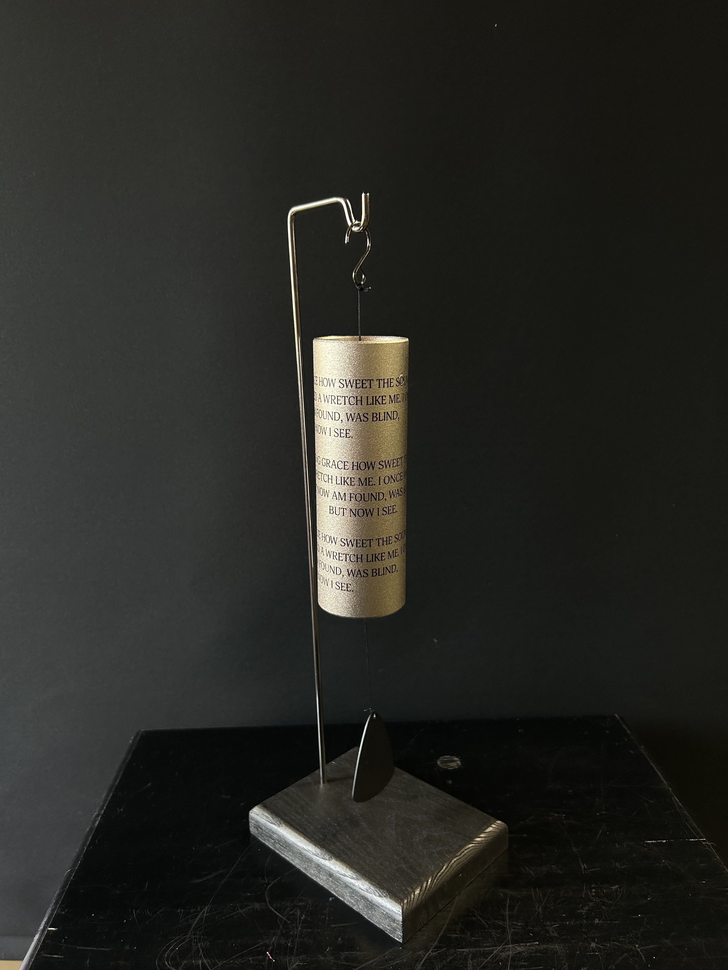 Gold wind chime hanging from a metal stand on a dark base