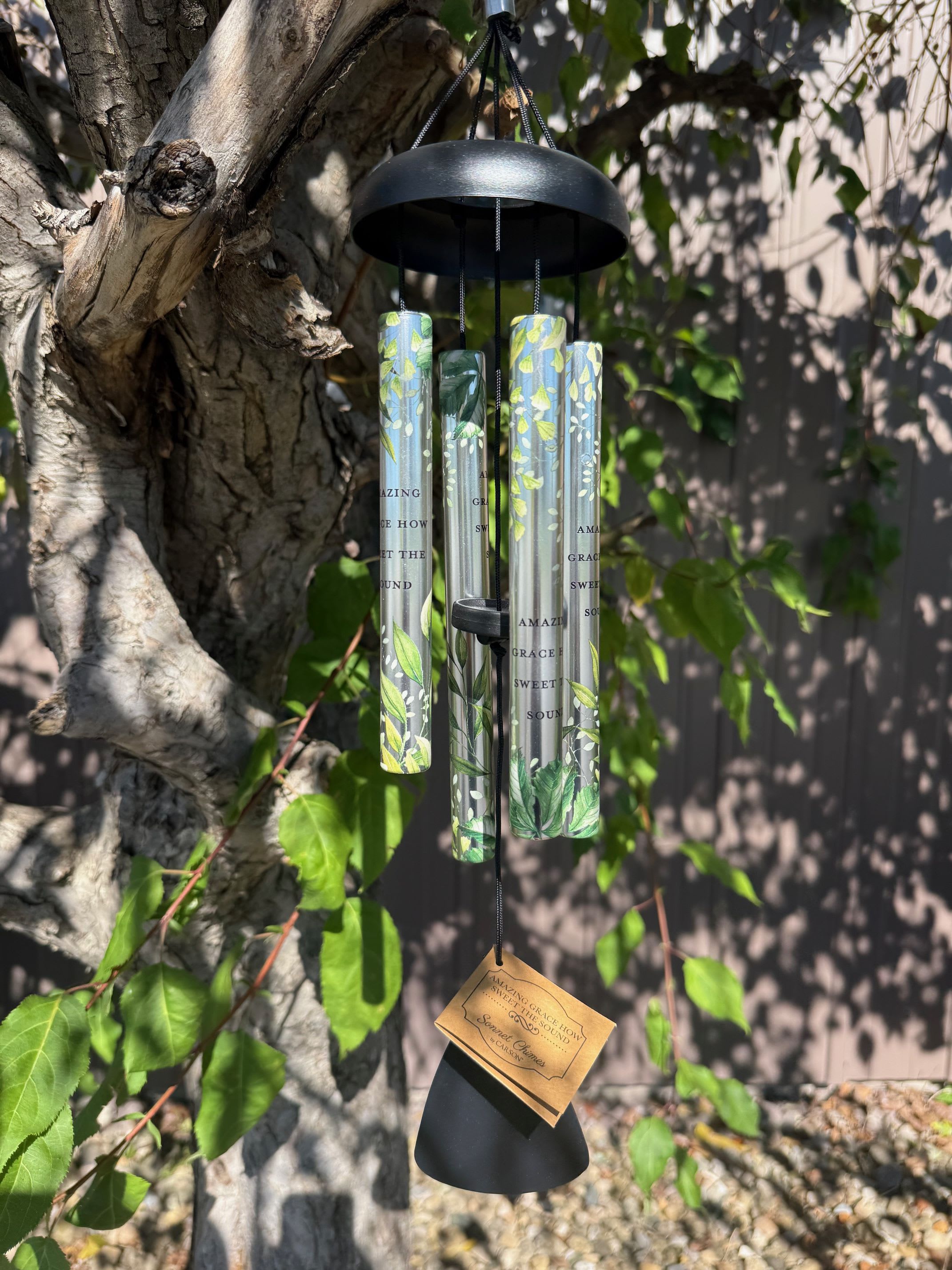 Black wind chime hanging from a tree with printed tubes and a tag
