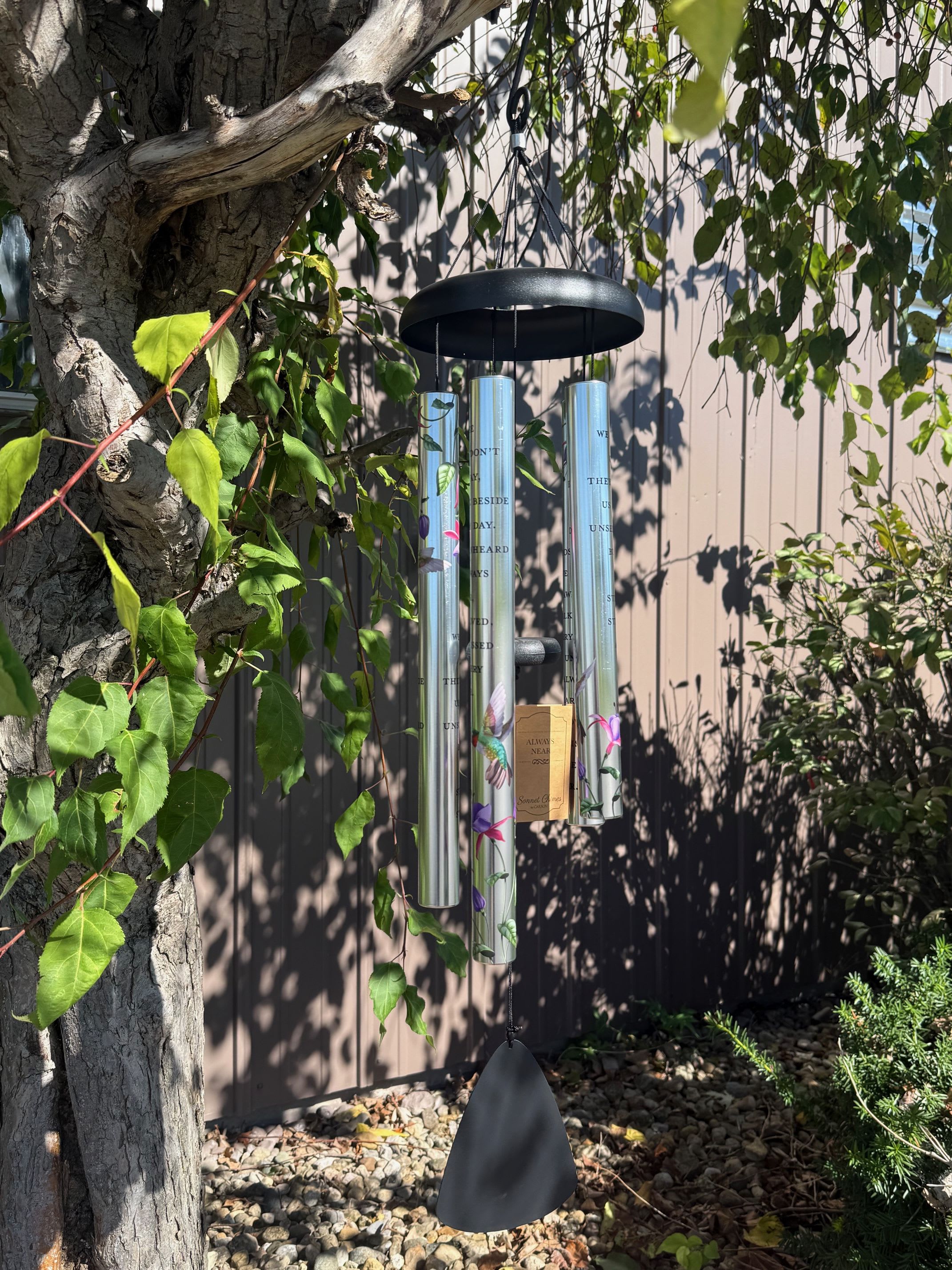 Hanging wind chime with silver tubes and a black top in a garden