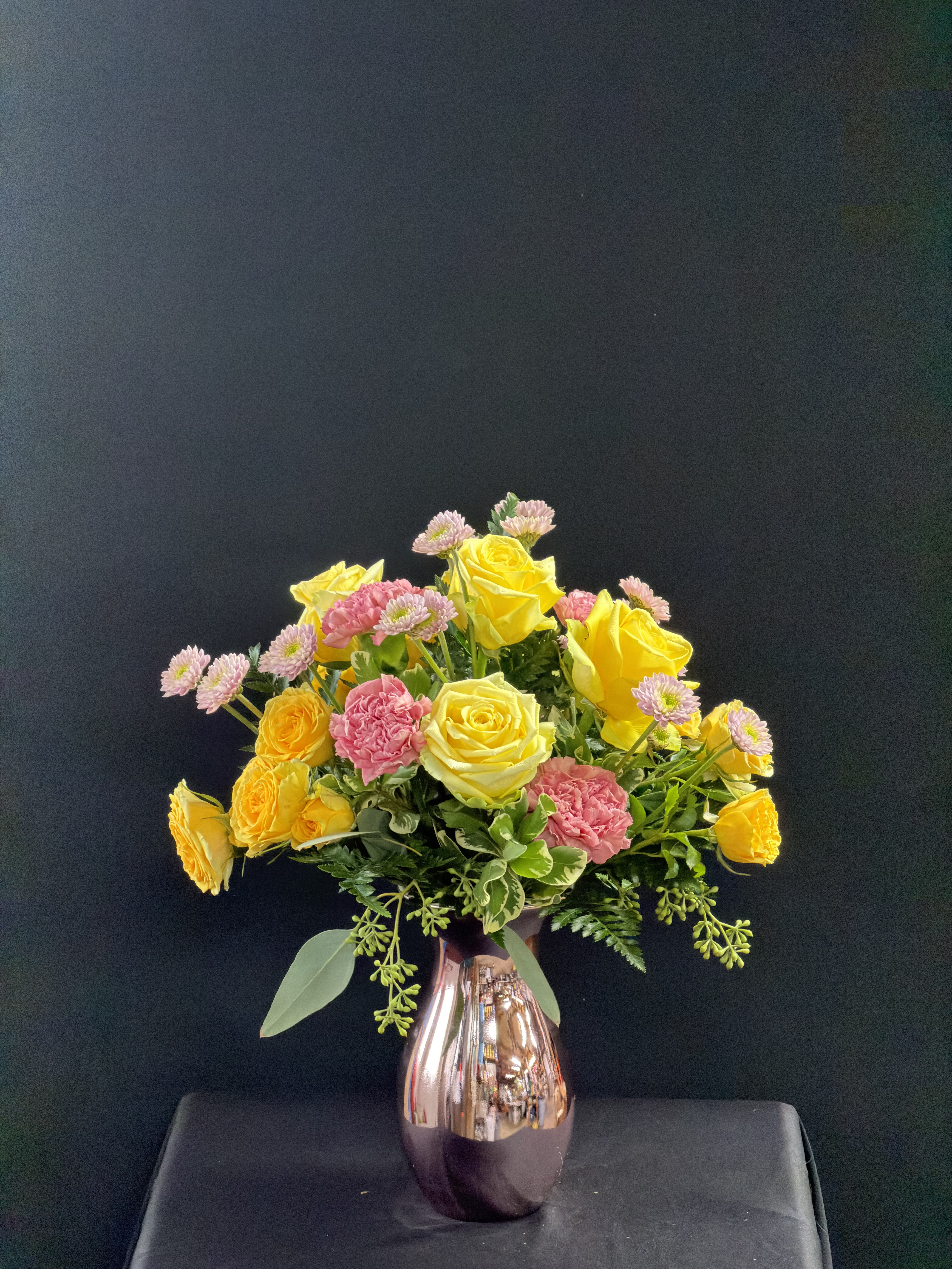 Yellow and pink roses with small pink daisies in a metallic vase