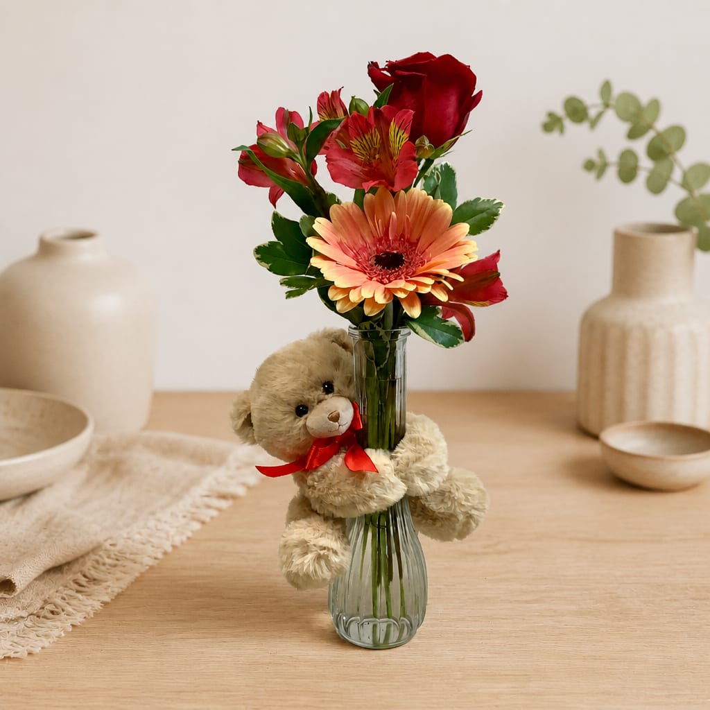 Bouquet of red and peach flowers in a glass vase with a teddy bear