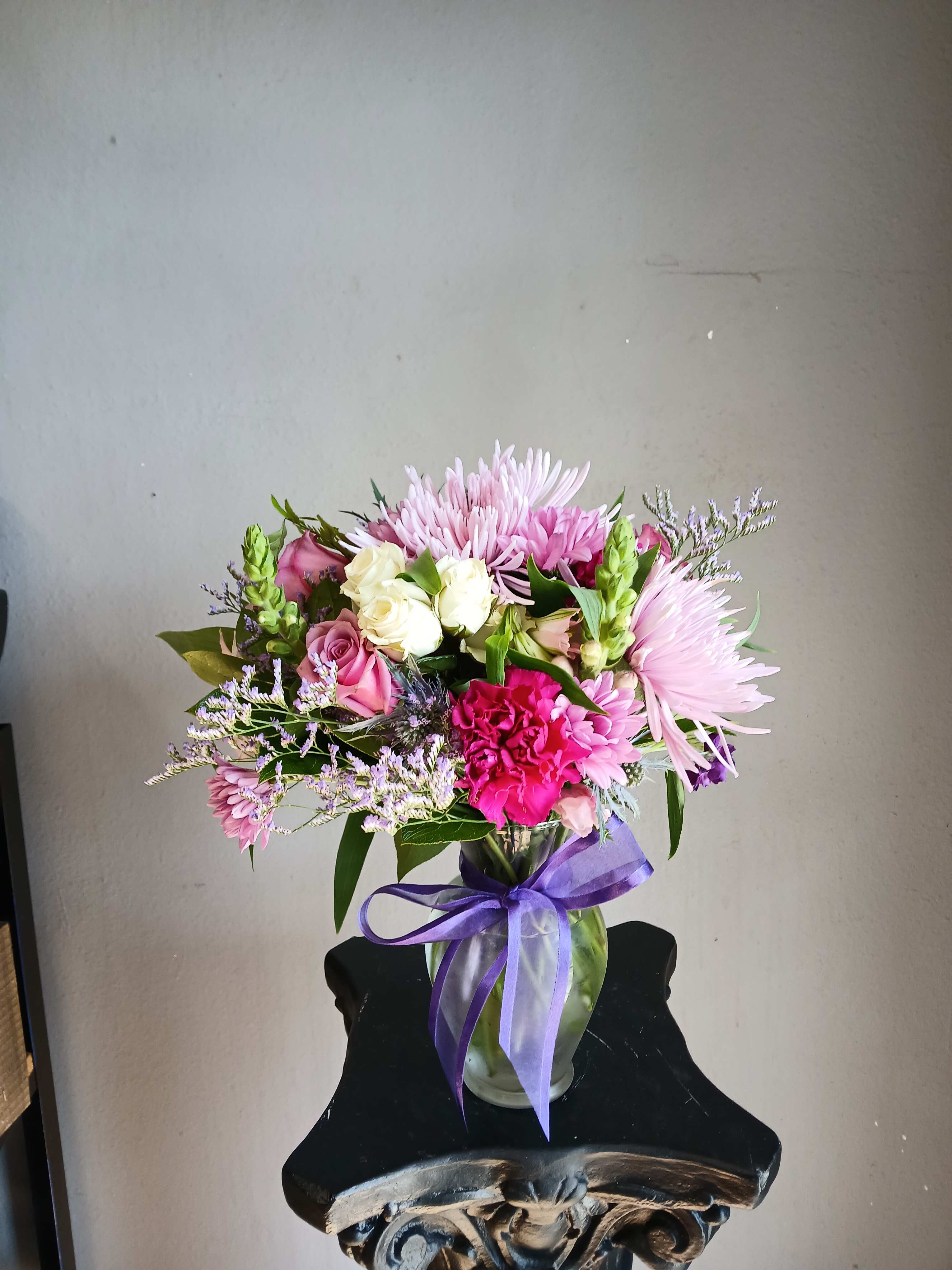 Pink and white mixed bouquet in a glass vase with a purple ribbon